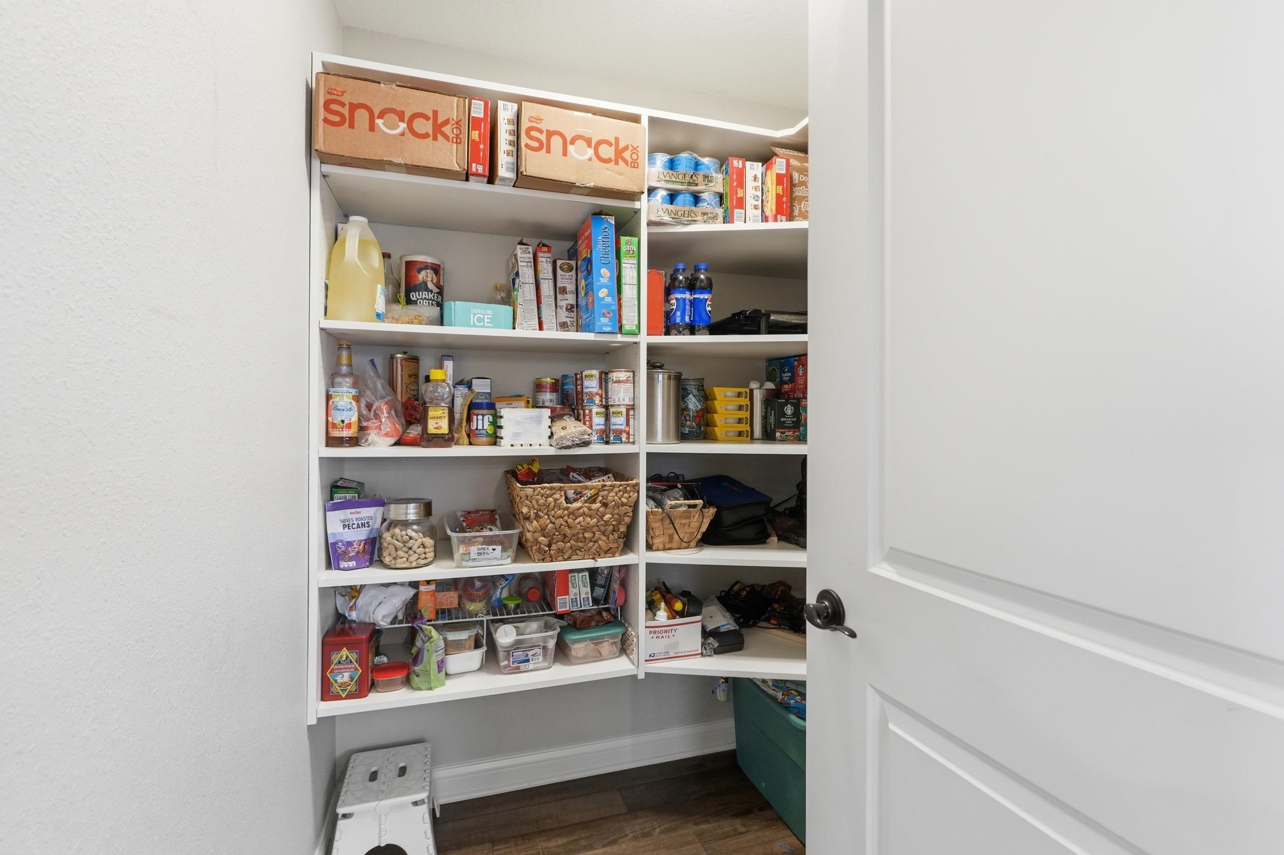 Spacious pantry featuring white built-in shelving, corner storage, and wood-finish flooring