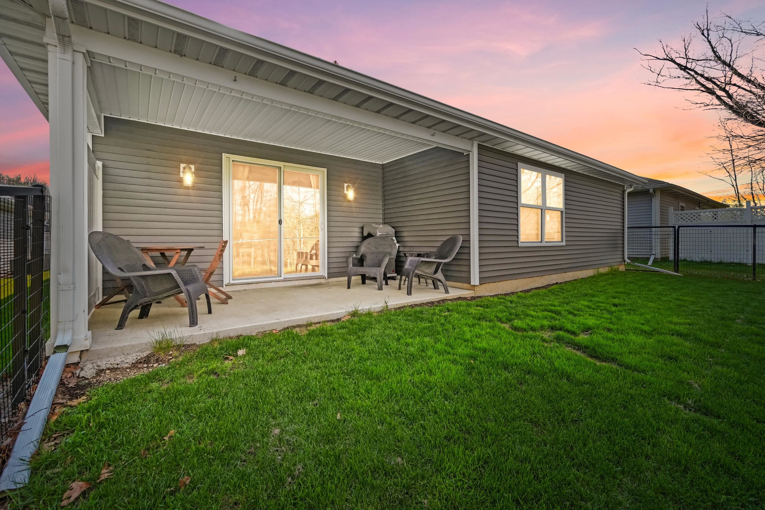 Covered concrete patio with two wall-mounted outdoor light fixtures, gray horizontal siding, and sliding glass doors