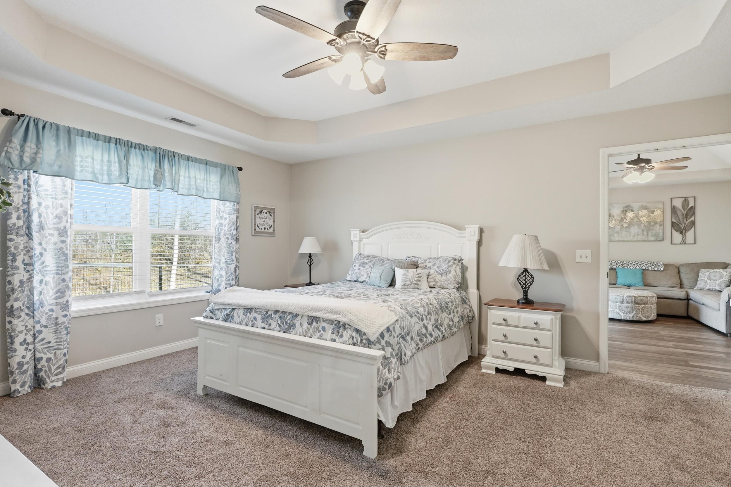 Carpeted room featuring a ceiling fan, tray ceiling, and a large window with white trim