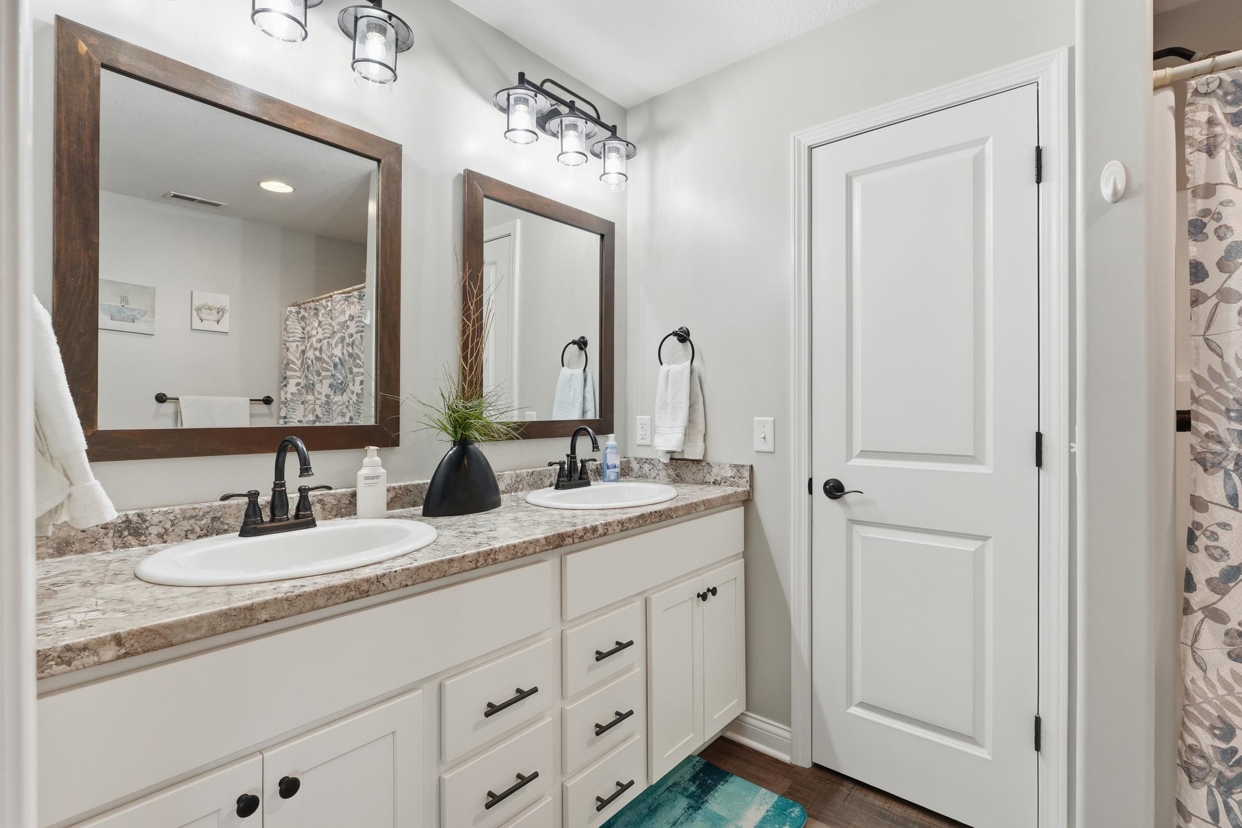 Double vanity with integrated sinks, granite-look countertop, white cabinetry with dark hardware, and two framed mirrors