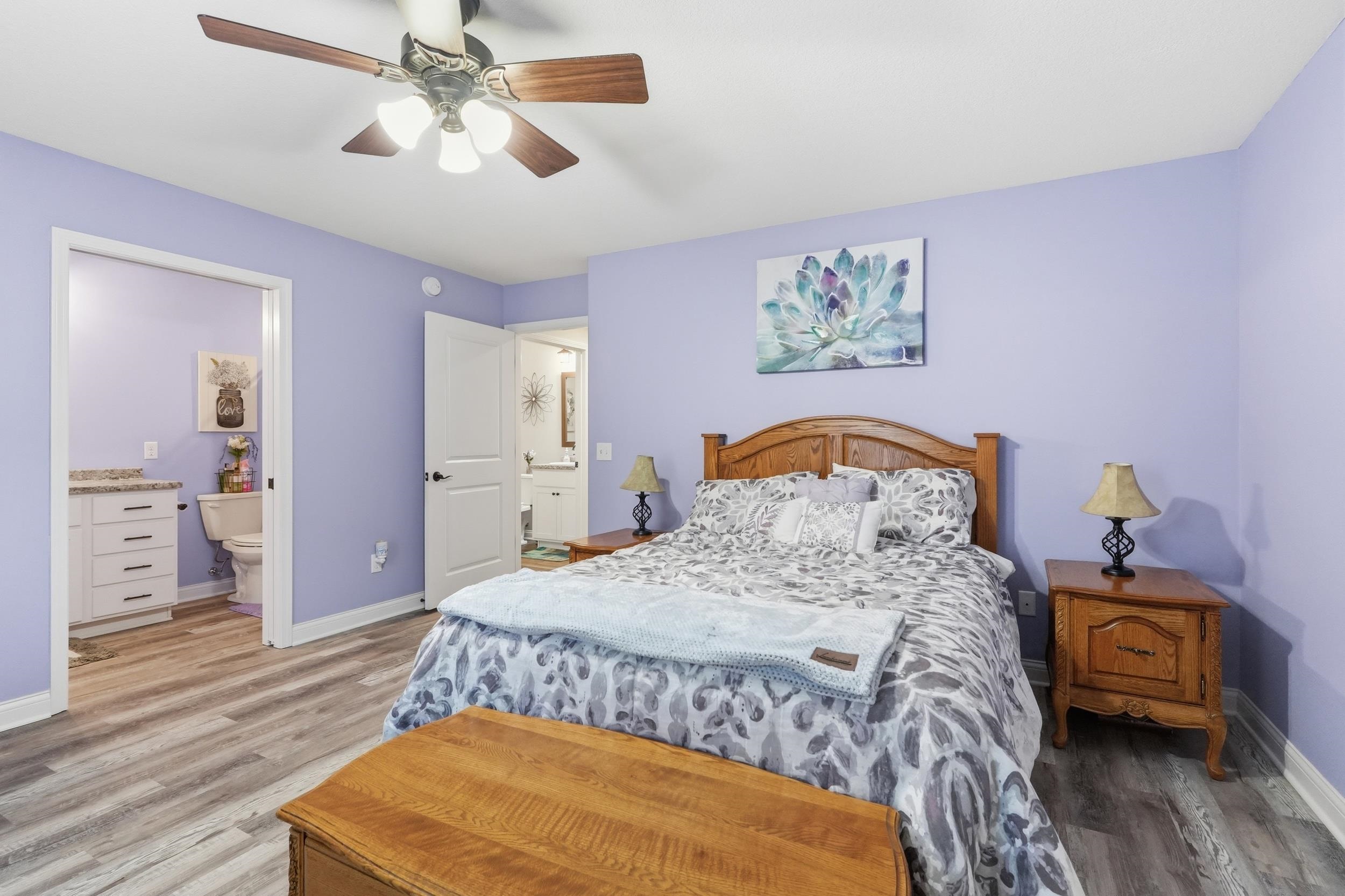 Bedroom featuring wood-finish flooring, a ceiling fan with integrated lighting, and a private three-piece bathroom with a white vanity and stone-look countertop