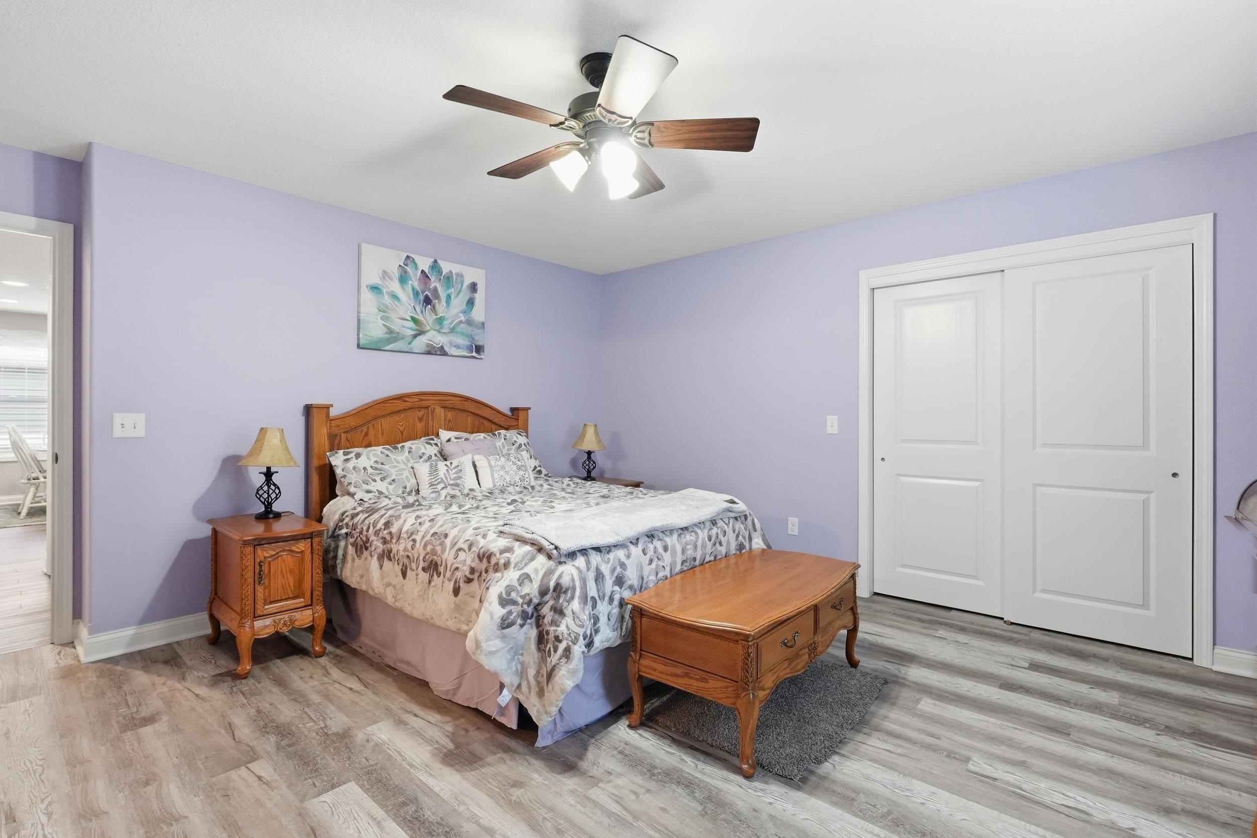 Room featuring wood-finish flooring, a ceiling fan with integrated lighting, and a closet with white bi-fold doors