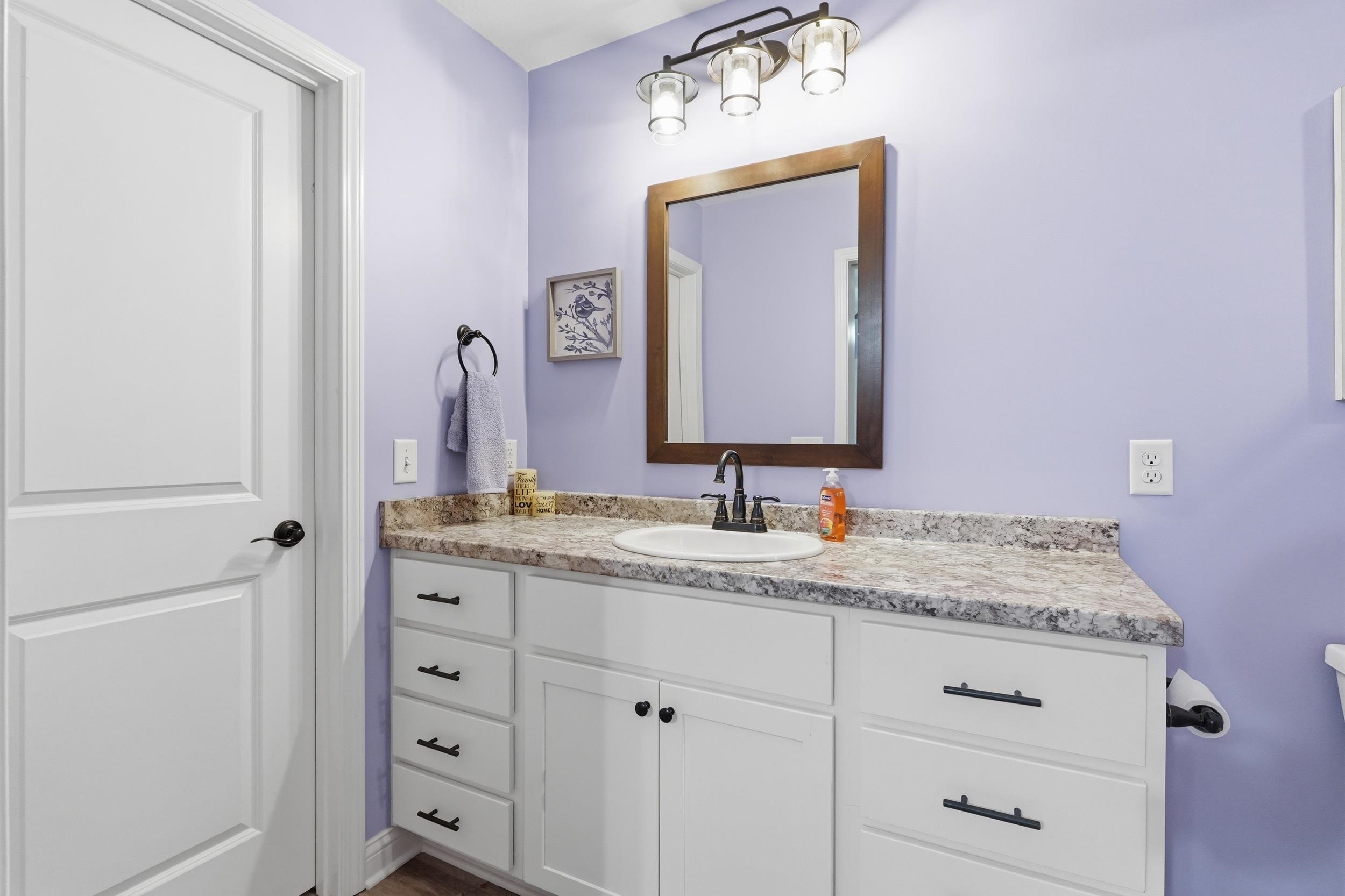 Bathroom featuring a white vanity with multiple drawers and cabinets, a speckled countertop, a rectangular sink with a matte black faucet, and a large wood-framed mirror