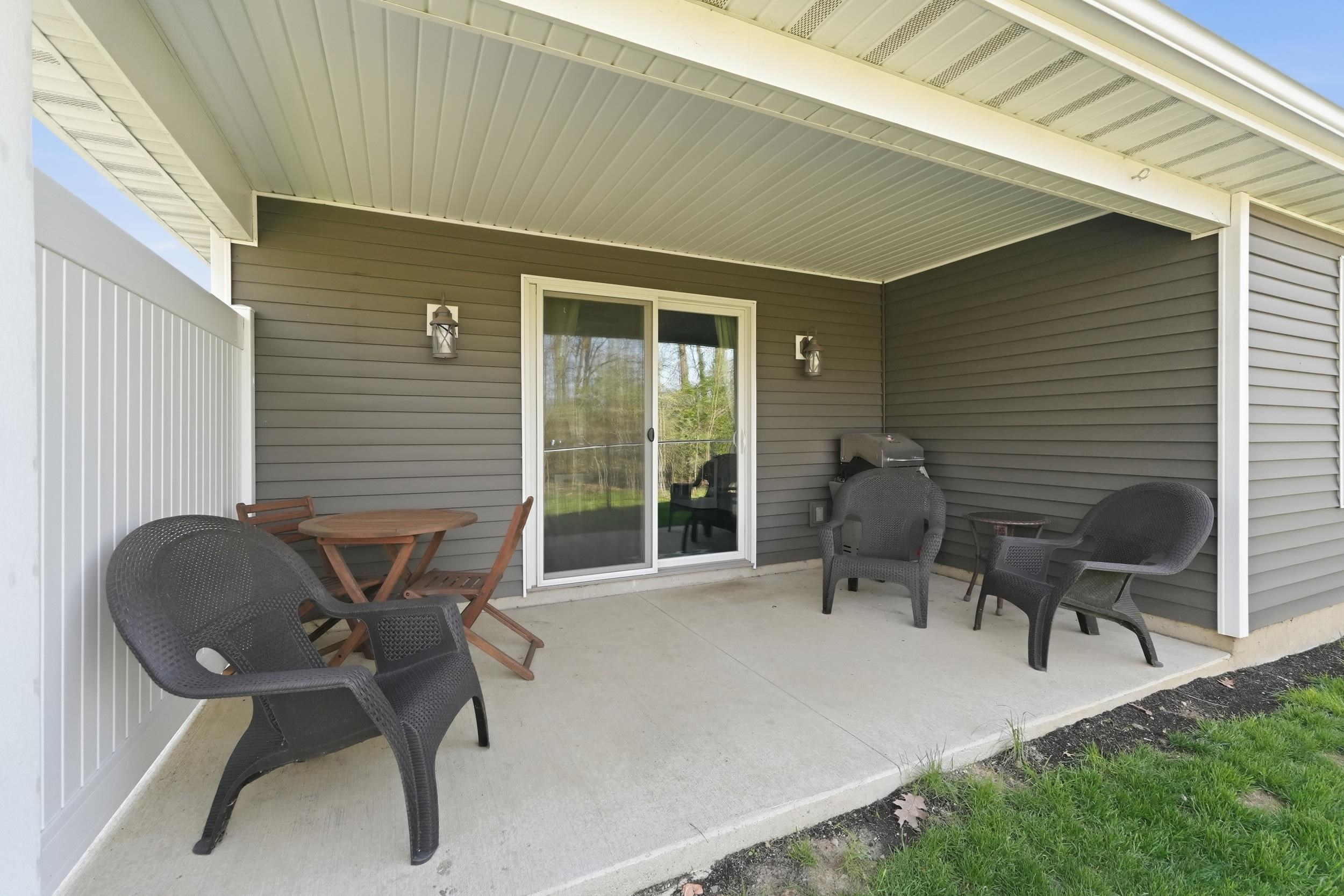Covered patio featuring a concrete slab, gray siding, white privacy fence, and sliding glass door access