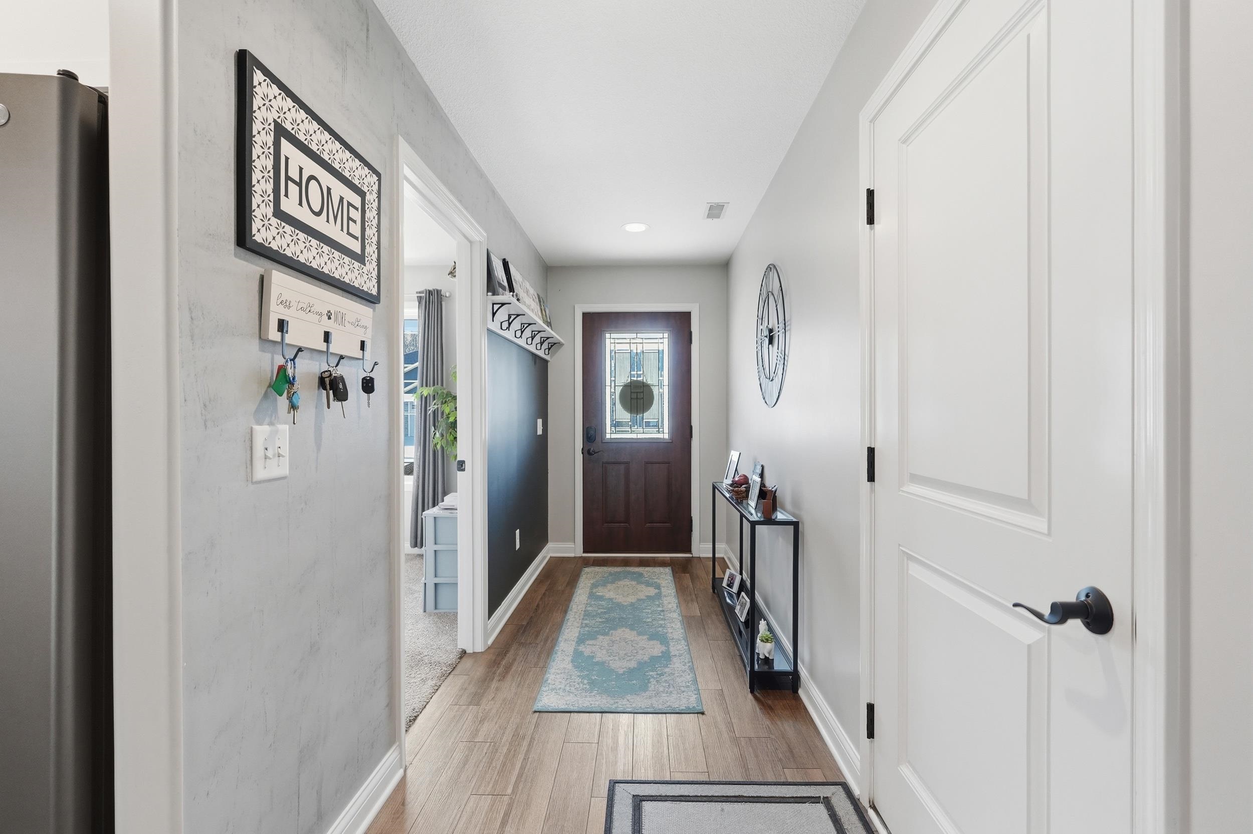 Entryway featuring wood-finish flooring, a dark wood entry door with leaded glass, white trim, and a built-in coat rack