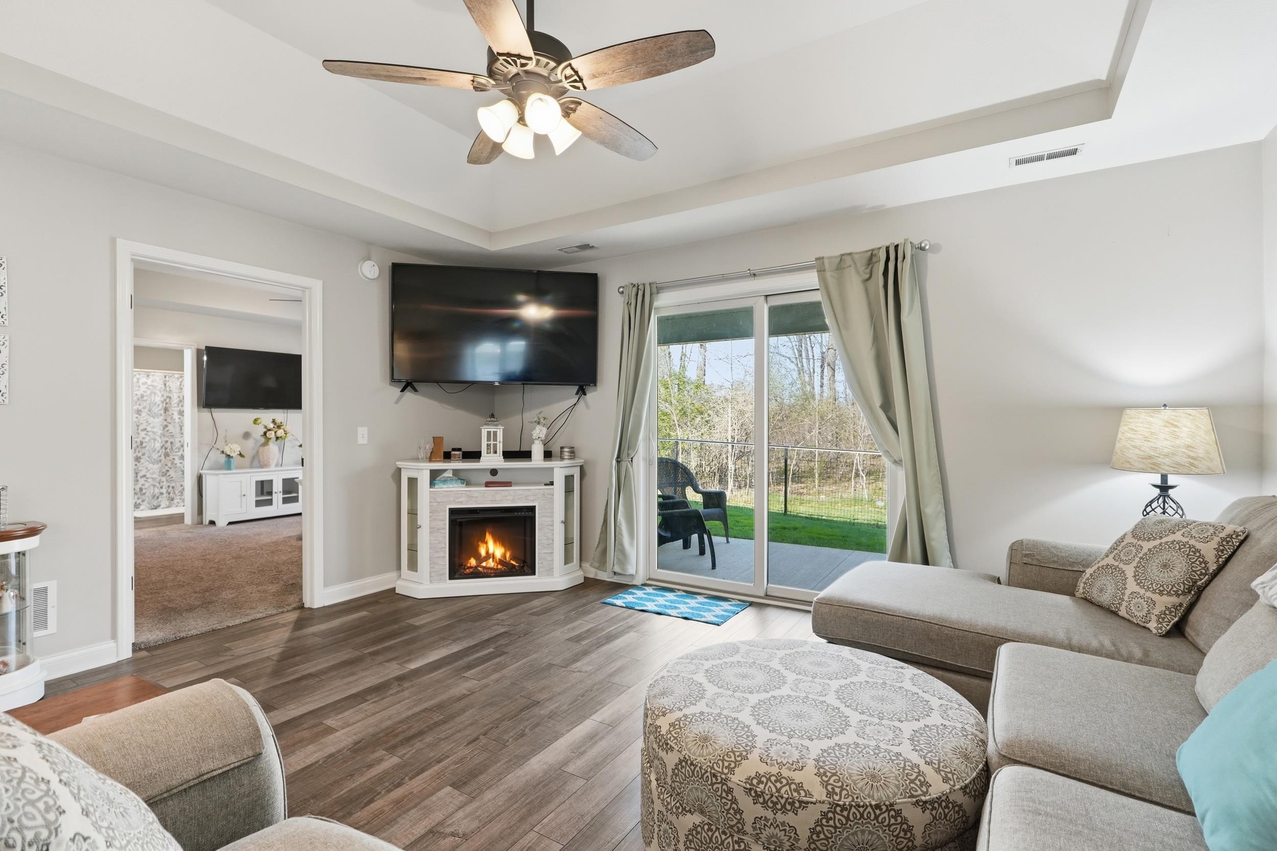 Spacious living area featuring wood-finish flooring, a corner-mounted electric fireplace, and a tray ceiling