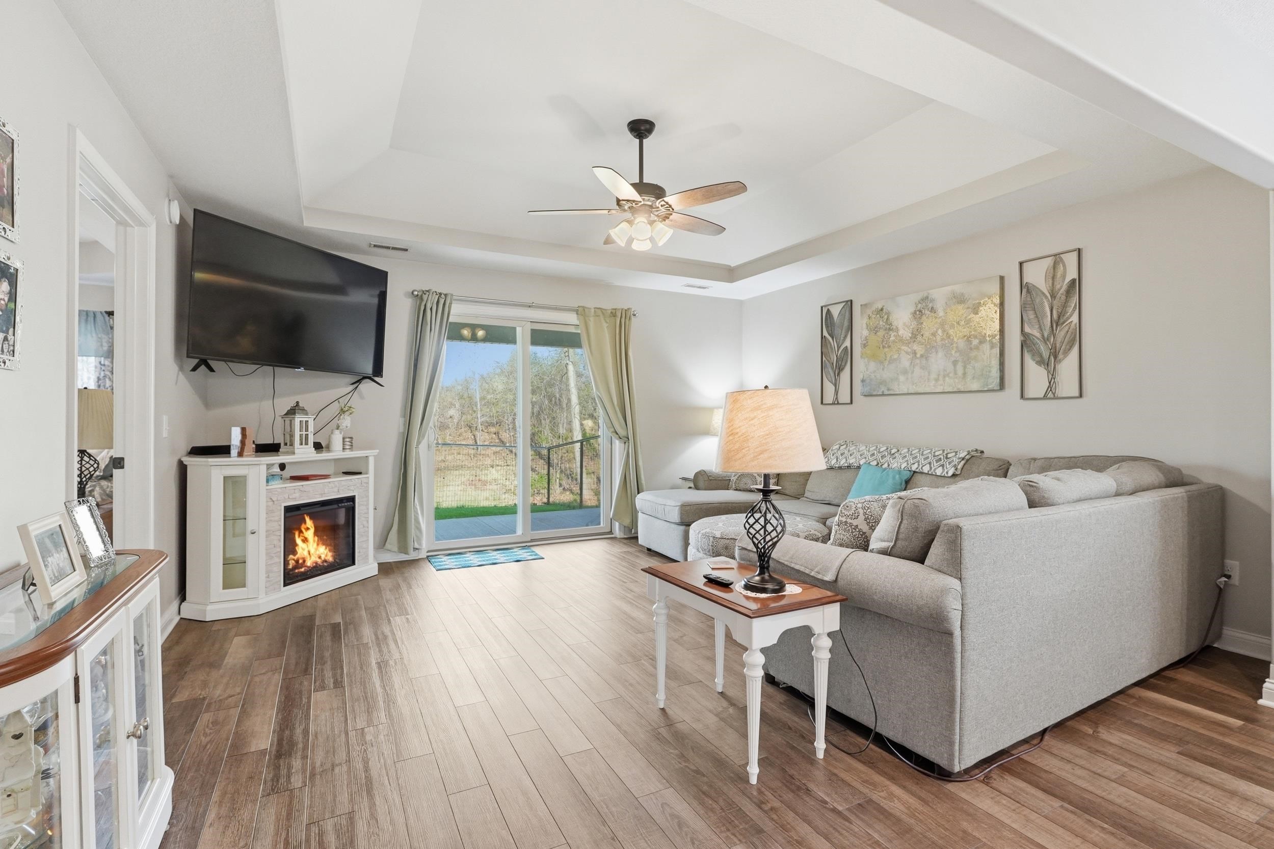 Spacious living area featuring wood-finish flooring, a corner-mounted electric fireplace, and a ceiling fan