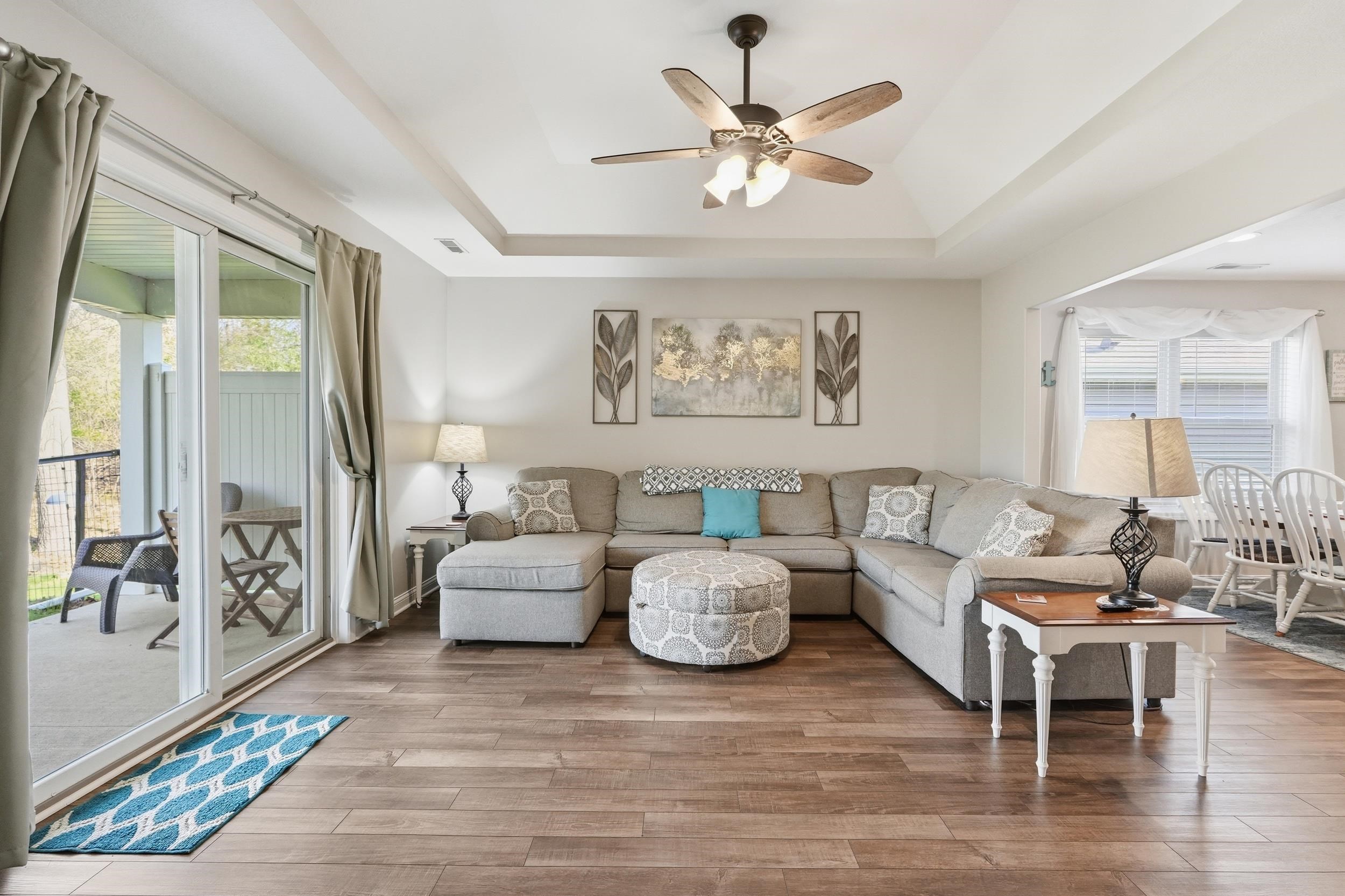Open-concept living space featuring wood-finish flooring, a tray ceiling with a ceiling fan, and sliding glass doors opening to an outdoor patio