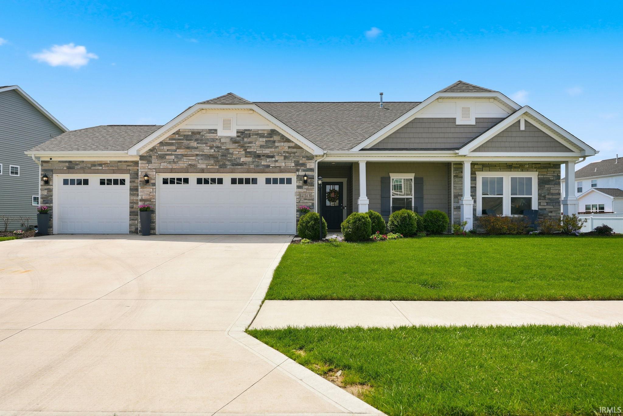 Ranch-style residence featuring a stone and siding facade, a two-car garage with individual doors, a covered front porch with white columns, and a concrete driveway