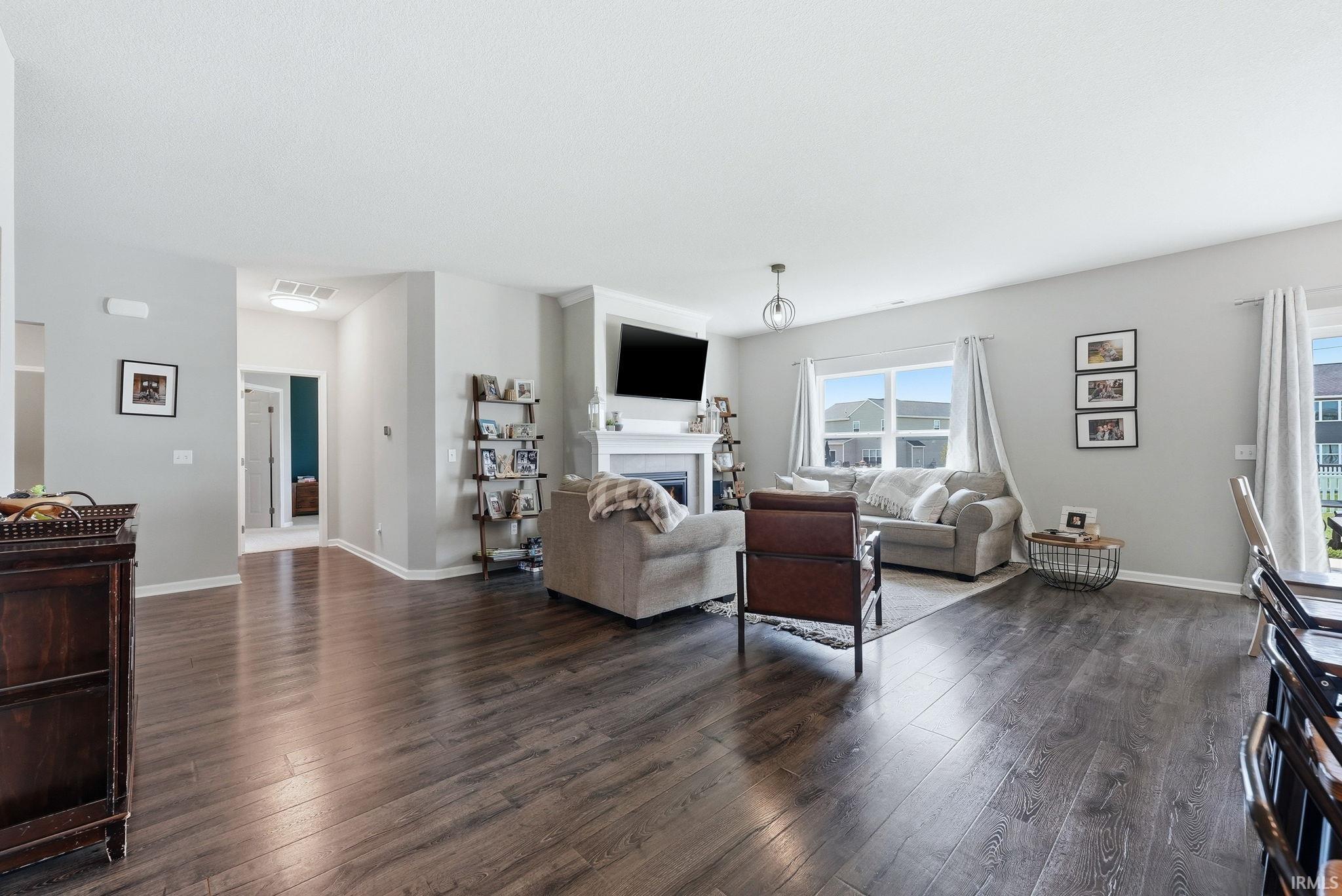 Spacious living area featuring dark wood-finish flooring, a white mantel fireplace, and ample natural light from multiple windows