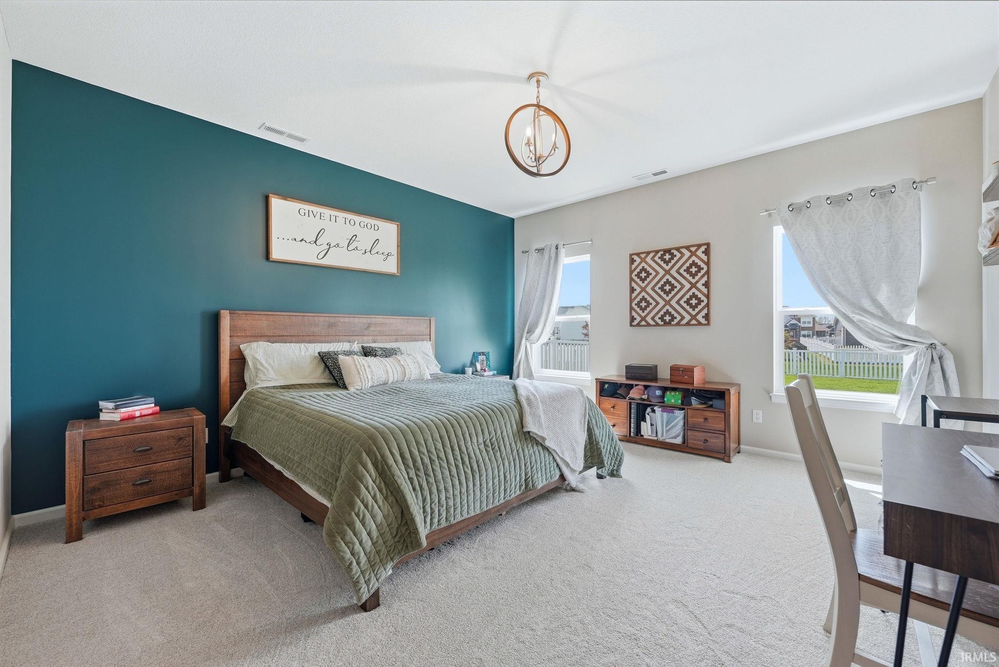 Spacious room featuring a teal accent wall, neutral carpeting, and two bright windows