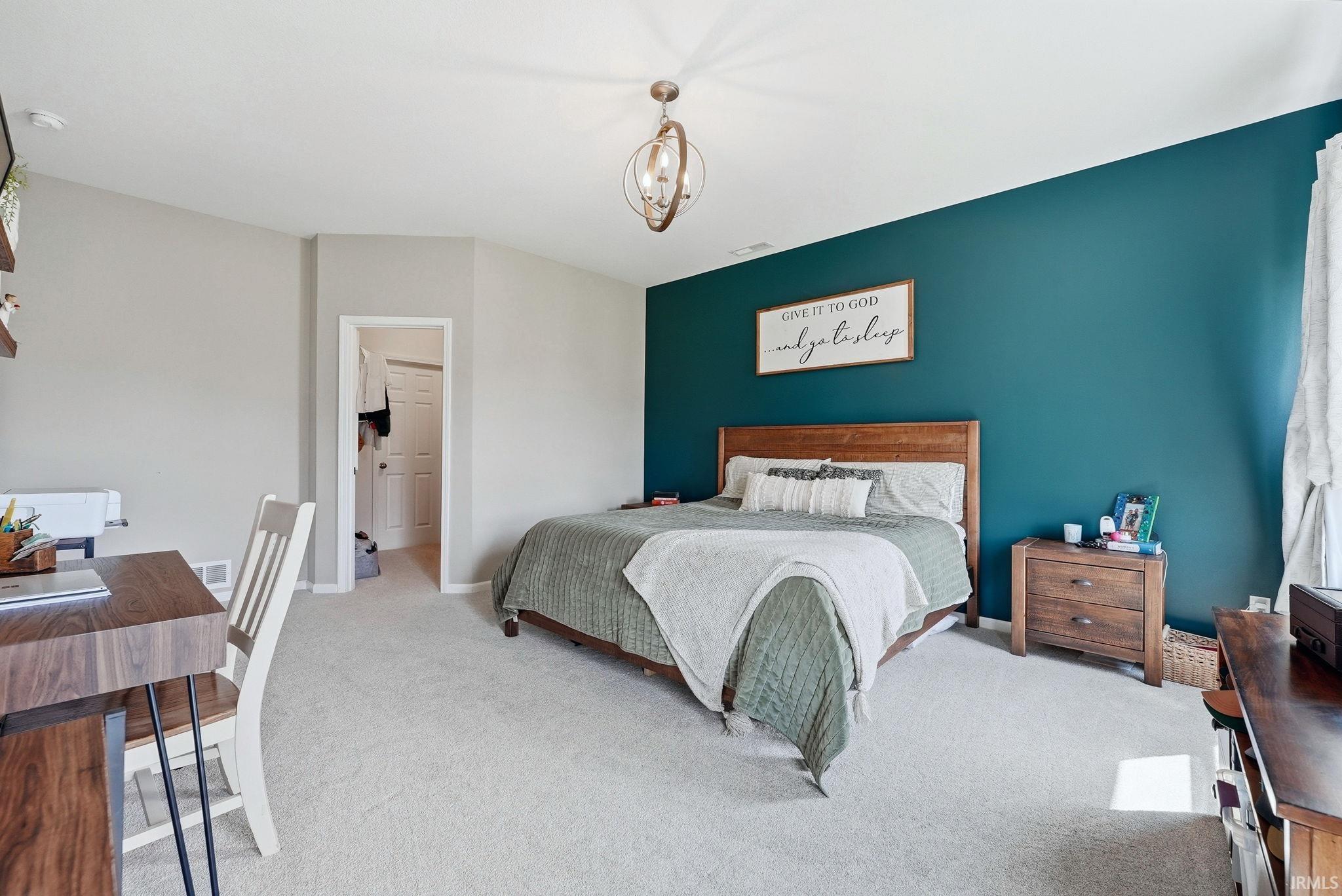 Carpeted bedroom featuring a vaulted ceiling with a semi-flush mount light fixture, accent wall, and wood-finish flooring in the doorway