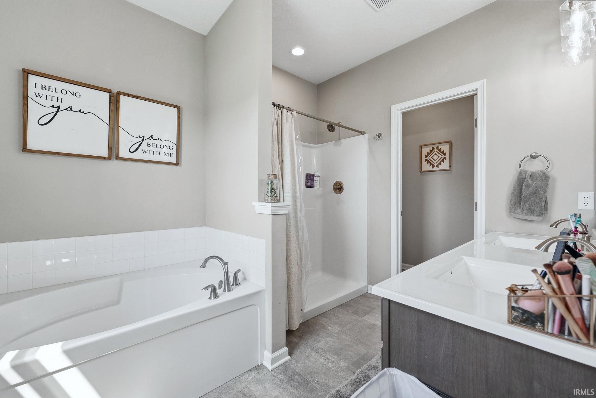 Bathroom featuring a built-in tub with tile surround, a separate shower enclosure, and a double vanity with an integrated countertop and sinks