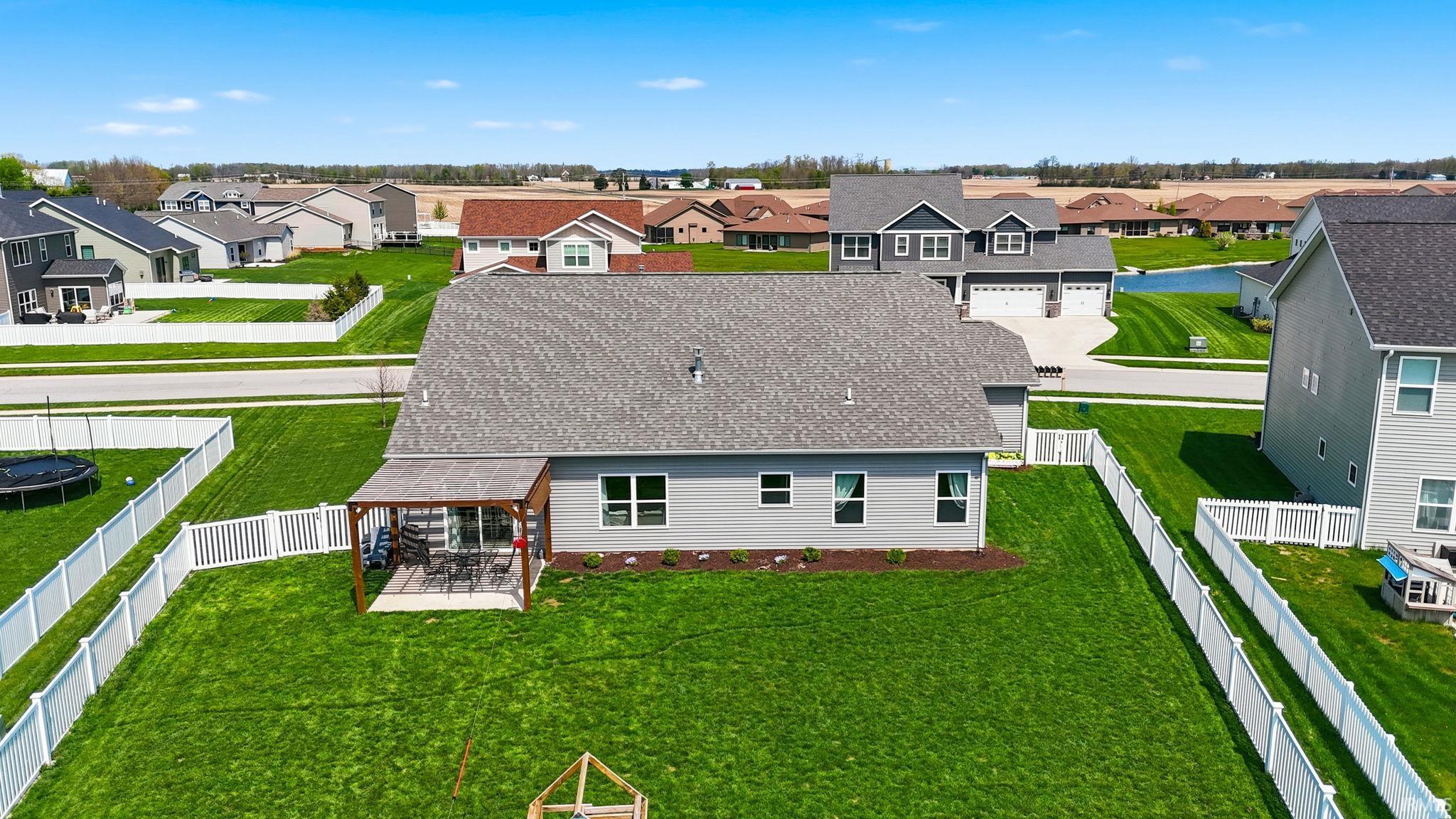 Expansive rear yard with a covered patio, manicured lawn, and white picket fencing