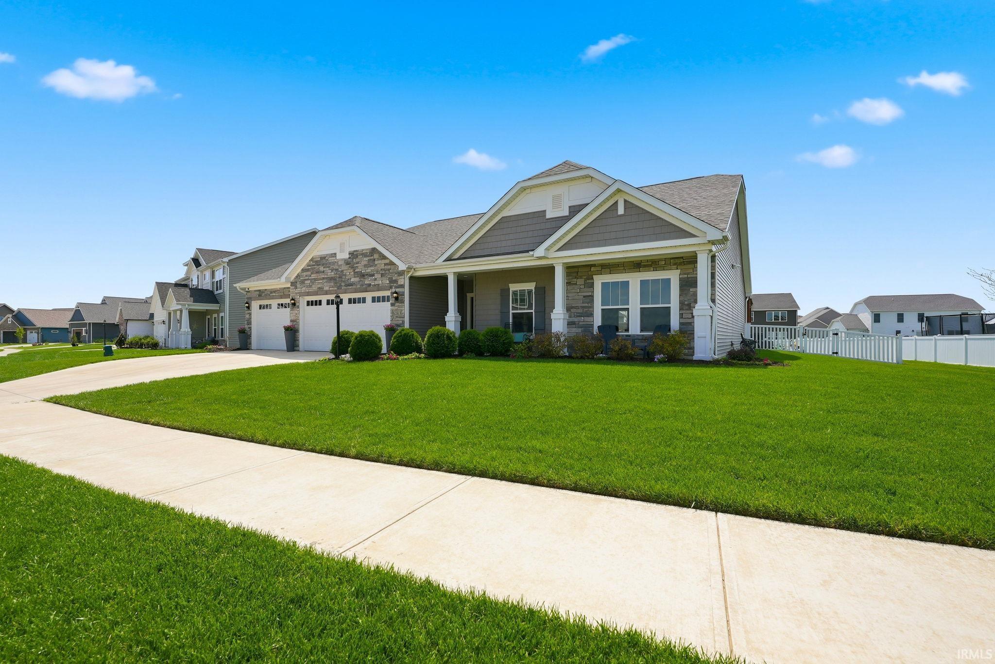 Modern ranch-style residence featuring a prominent two-car garage, stone and siding exterior, a covered porch, and a concrete driveway