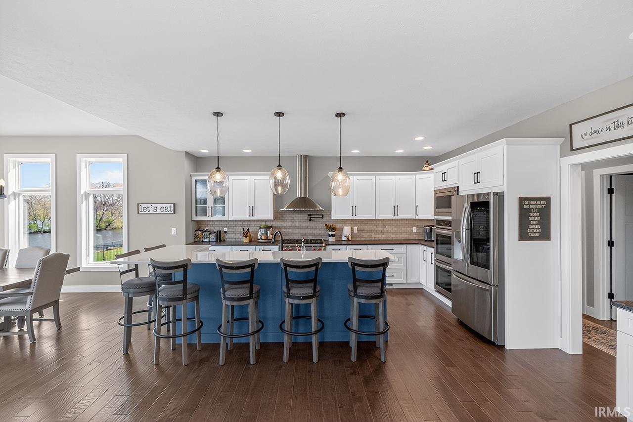 Gourmet kitchen featuring a large central island with seating, stainless steel appliances, white cabinetry with dark hardware, a tile backsplash, and wood-finish flooring