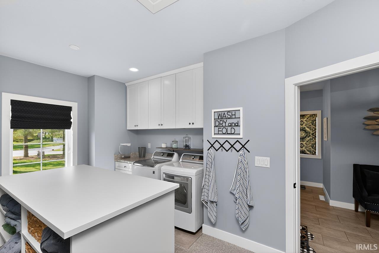 Main suite walk in closet with dedicated laundry space featuring a large central island, white cabinetry, and a window with natural light