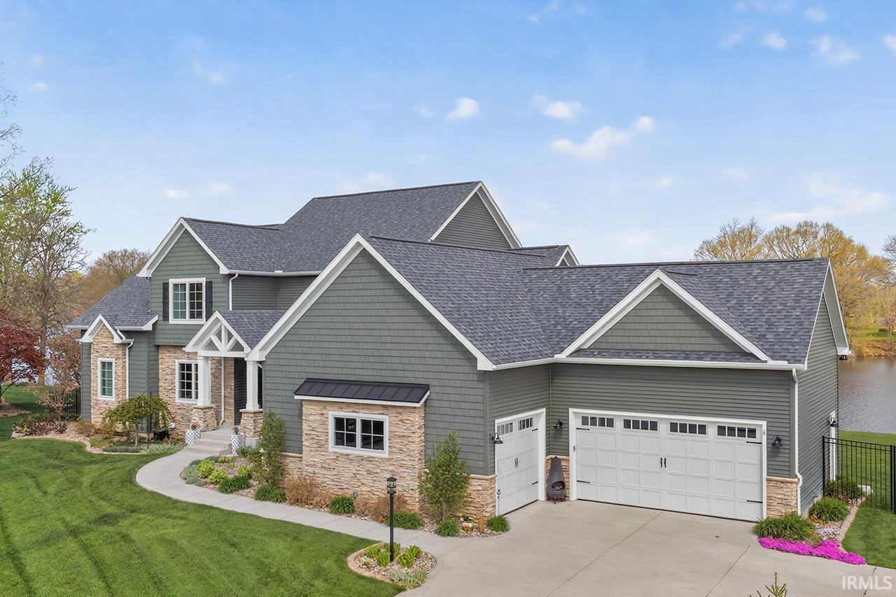Two-story residence featuring green siding, stone accents, and a multi-car garage with white doors