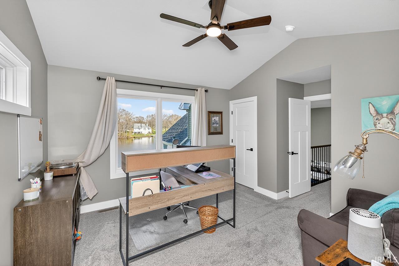 Vaulted ceiling room featuring a large window with water views, a multi-speed ceiling fan, neutral gray walls, and white paneled doors