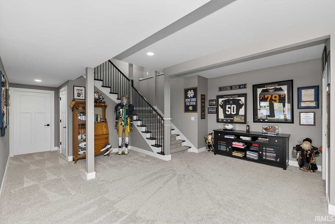 Spacious lower level featuring light gray carpeting, neutral wall colors, recessed lighting, white trim, and a staircase with black metal balusters
