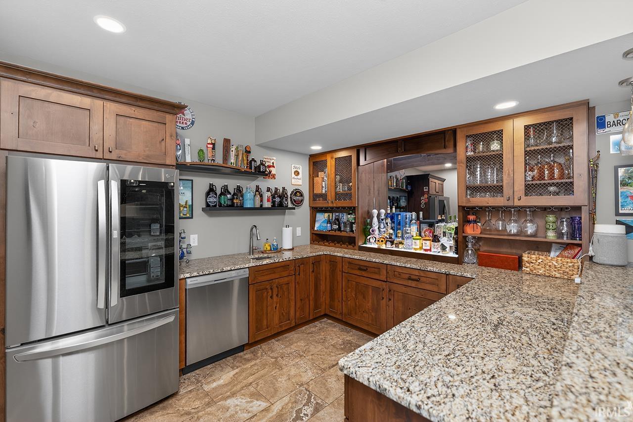 Custom wet bar featuring wood cabinetry, granite countertops, stainless steel appliances, and integrated lighting
