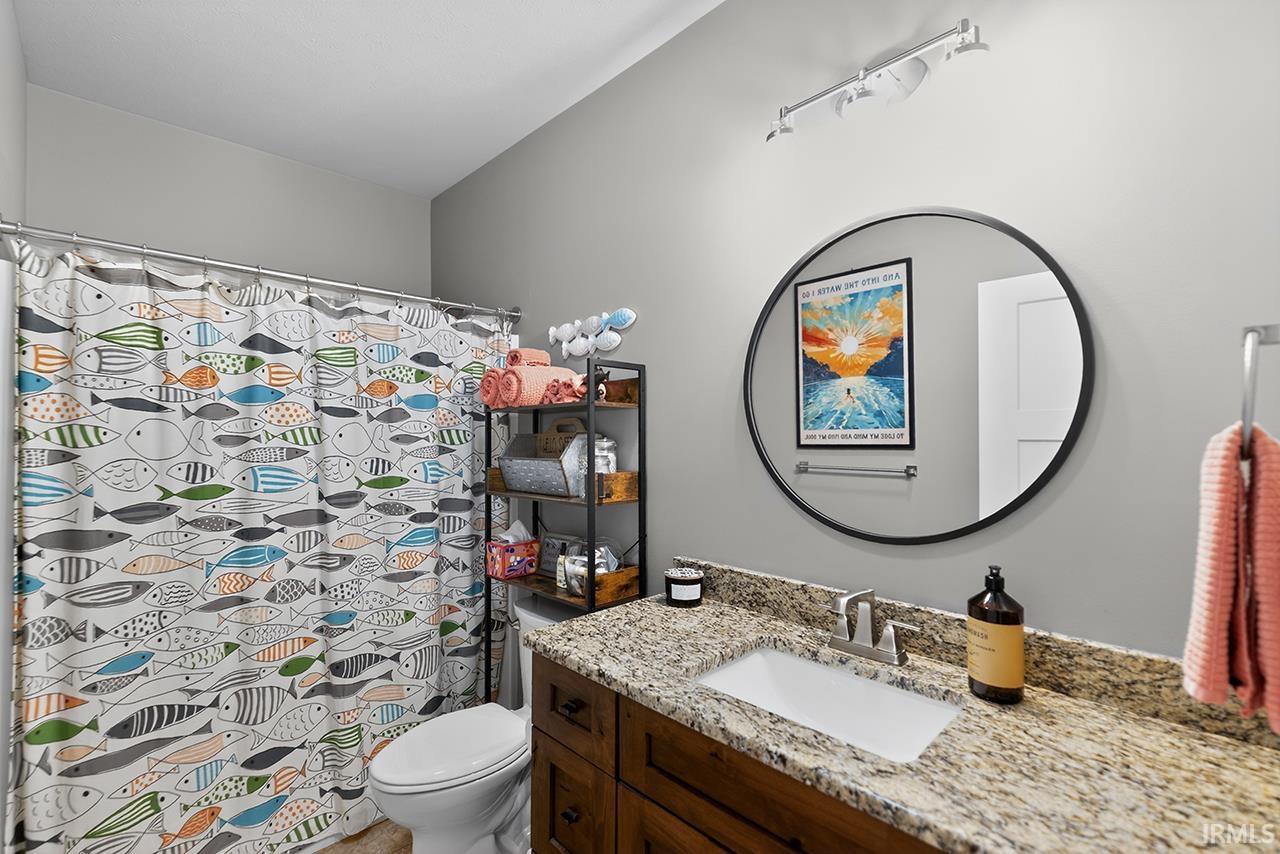 Bathroom featuring a shower with a privacy curtain, granite-style countertop, undermount sink, wood-finish vanity cabinetry, and a circular wall mirror