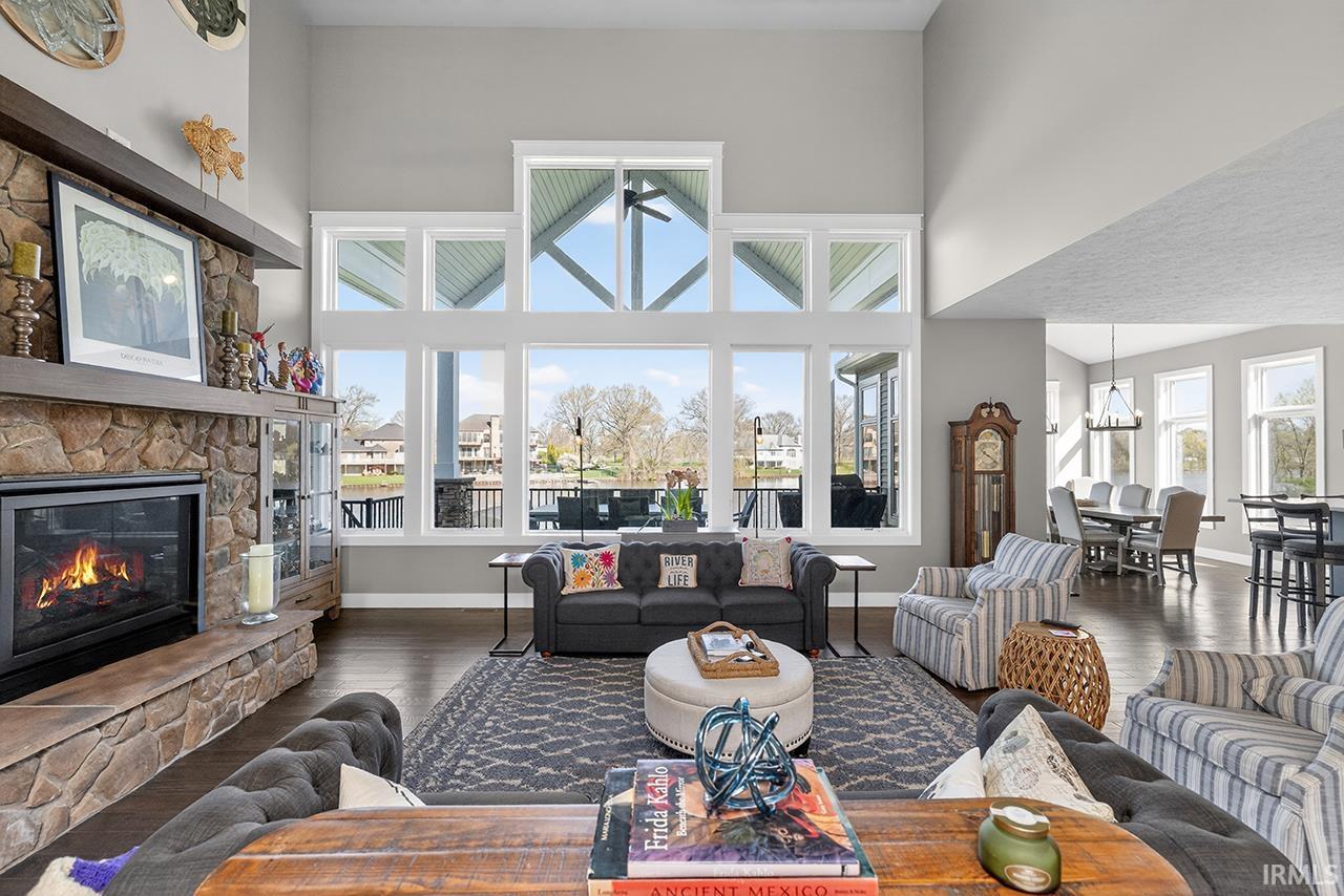 Spacious living area featuring expansive floor-to-ceiling windows, a stone-faced fireplace with a wood mantel, vaulted ceilings, wood-finish flooring, and an open-concept layout into a dining area