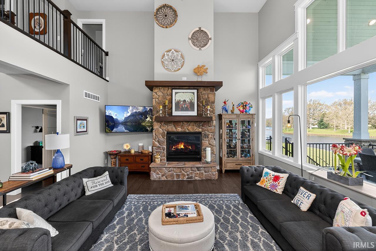 Great room featuring a floor-to-ceiling stone fireplace with a wood mantle, high ceilings, dark wood-finish flooring, and a second-story interior balcony with dark wood railings