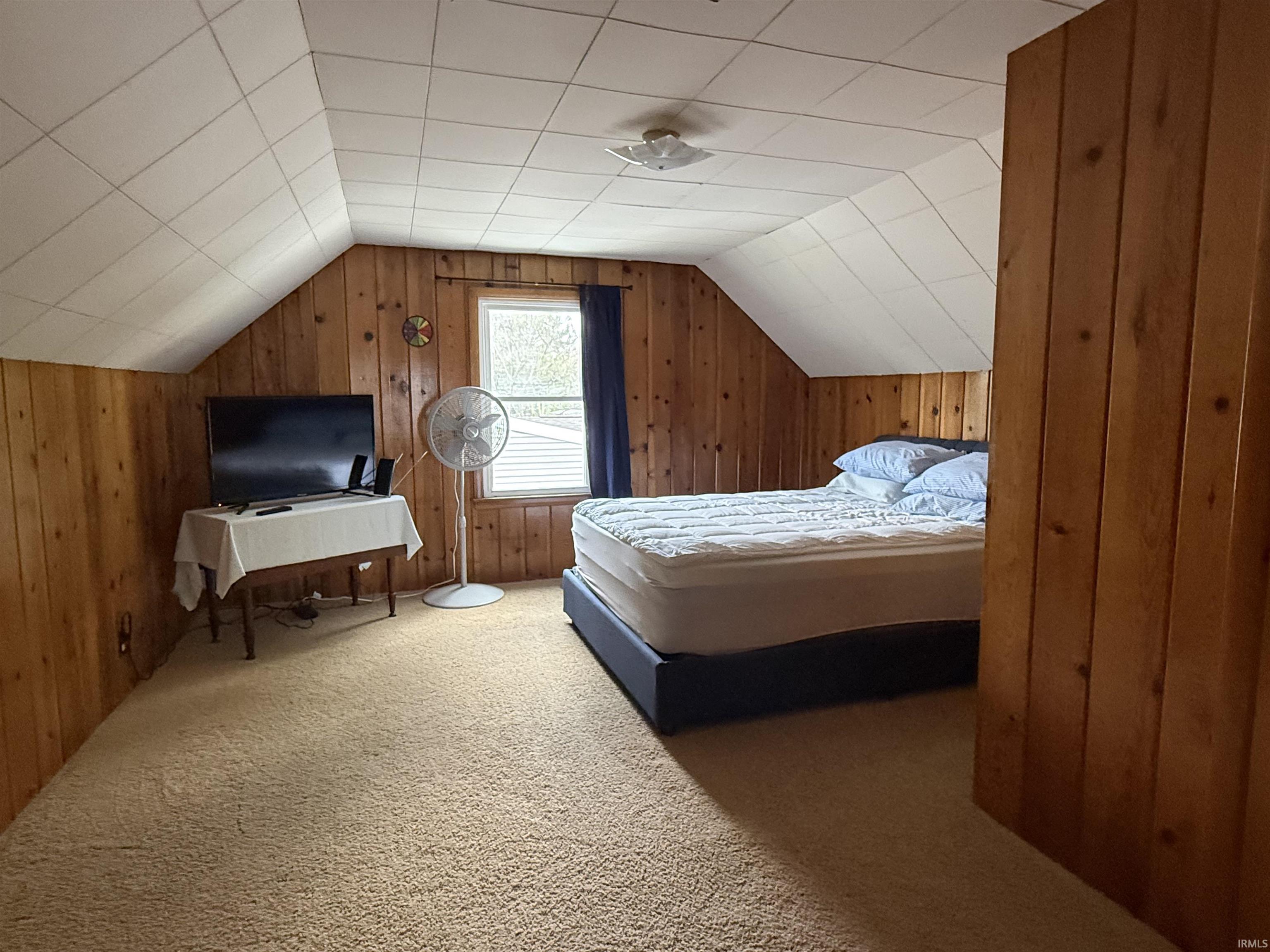 Carpeted room featuring natural wood paneling, a sloped ceiling with acoustic tiles, and a single window with dark blue drapes