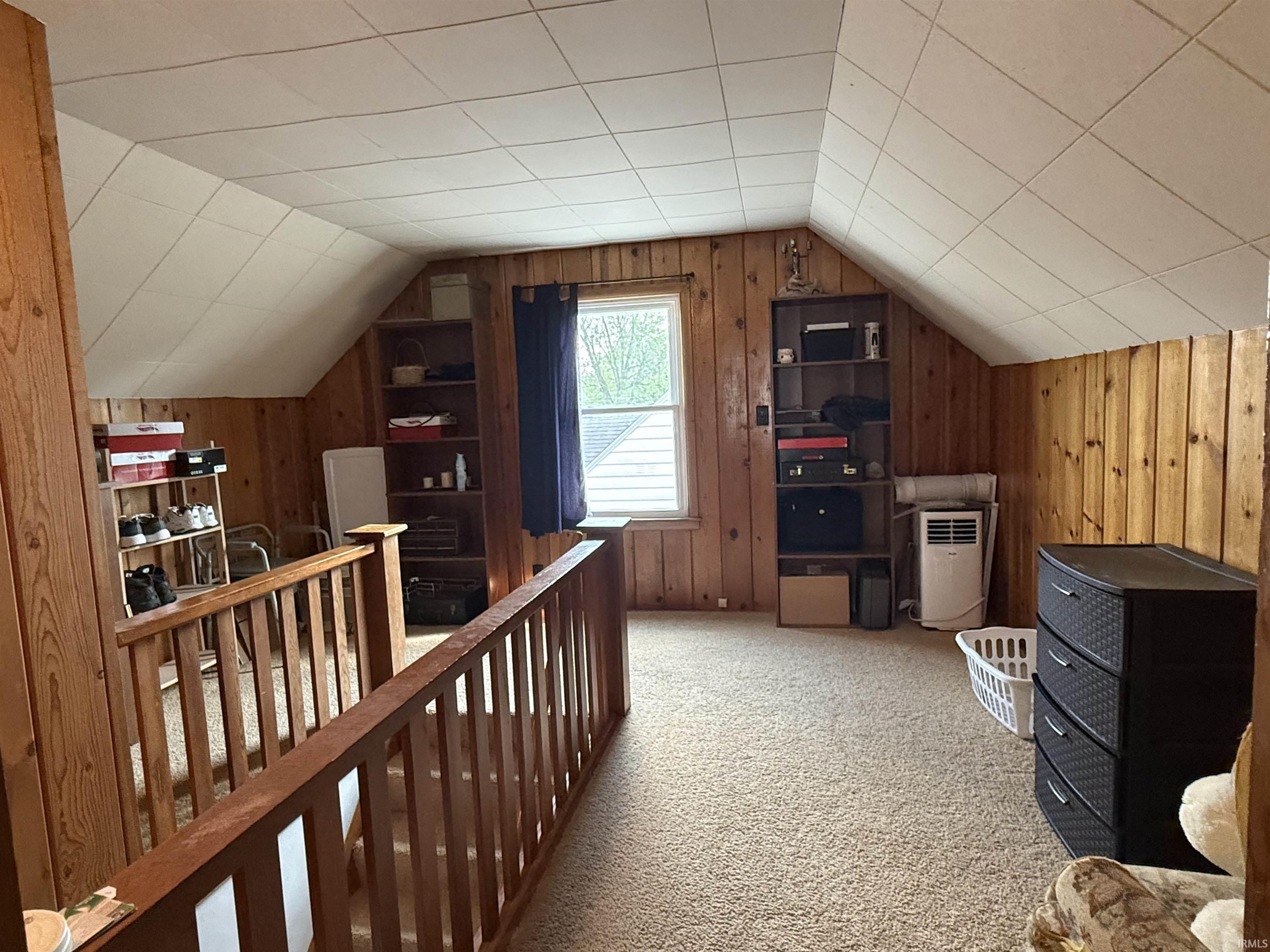 Carpeted loft area featuring wood paneling, sloped ceilings with ceiling tiles, and a window for natural light
