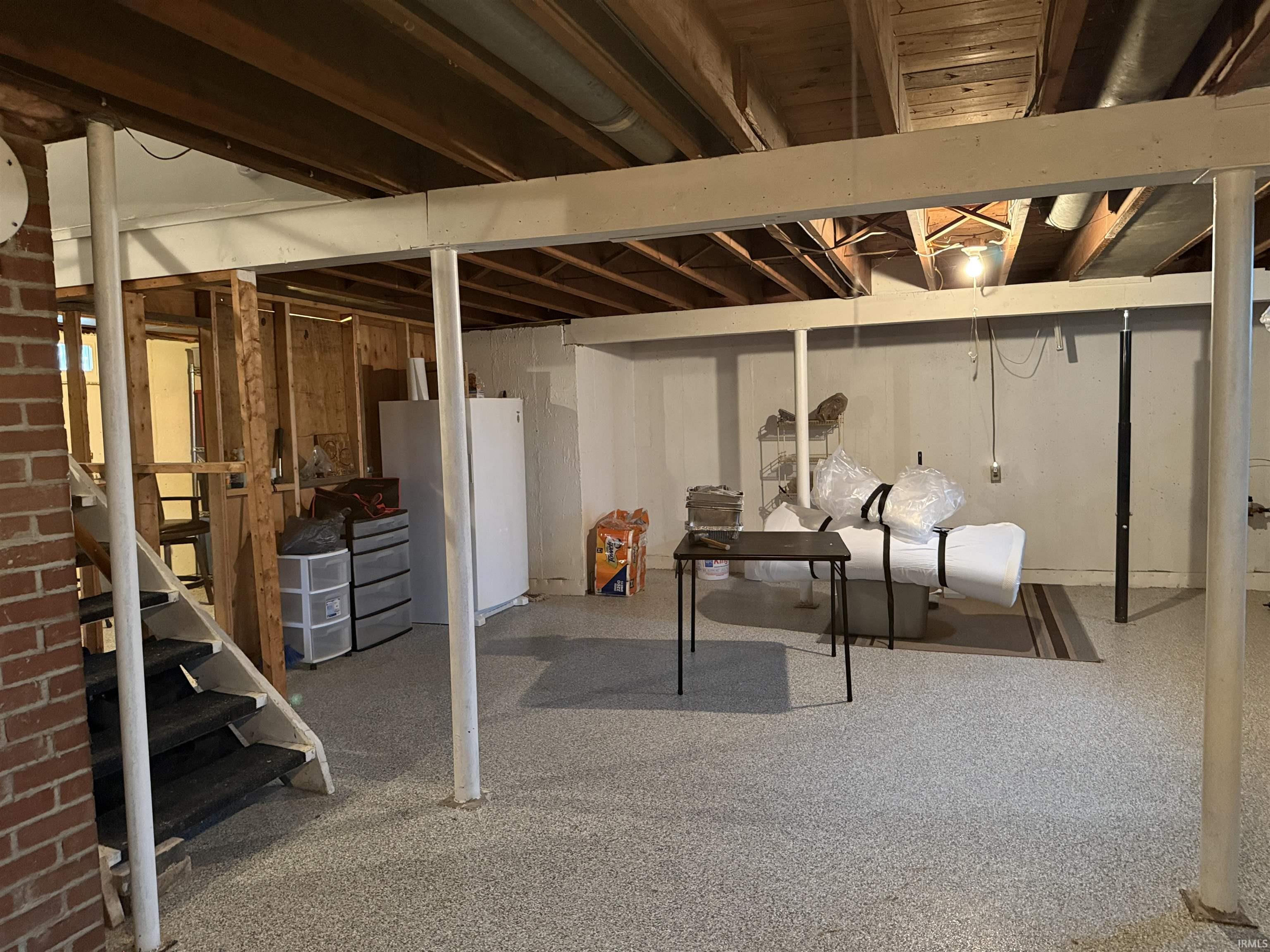 Unfinished basement featuring exposed wood joists, brick detailing, and a partially framed room