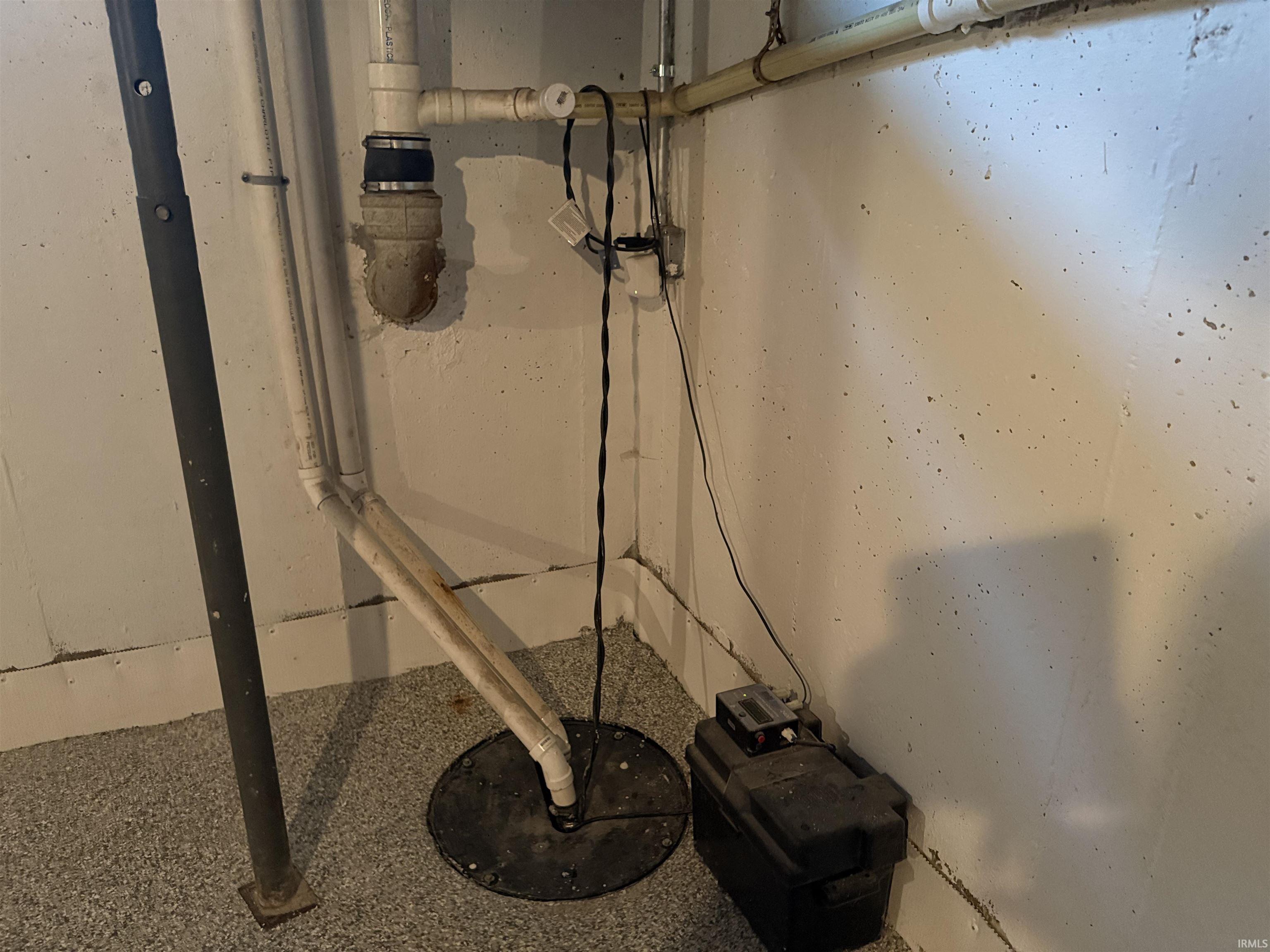 Sump pump system with white PVC drainage piping and an associated battery backup unit