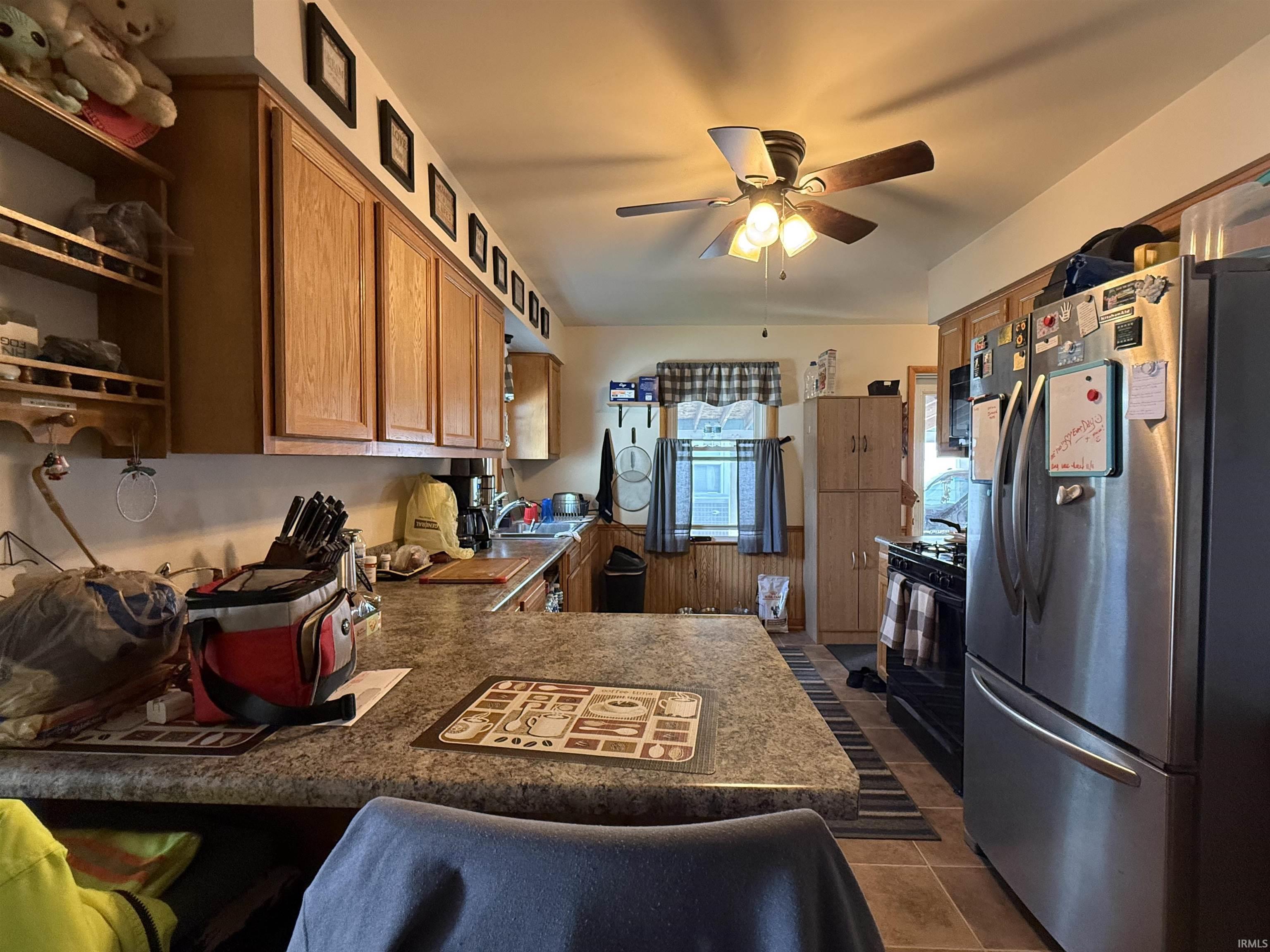 Kitchen featuring extensive cabinetry, a ceiling fan with integrated lighting, a stainless steel refrigerator, a black range, and stone-finish countertops