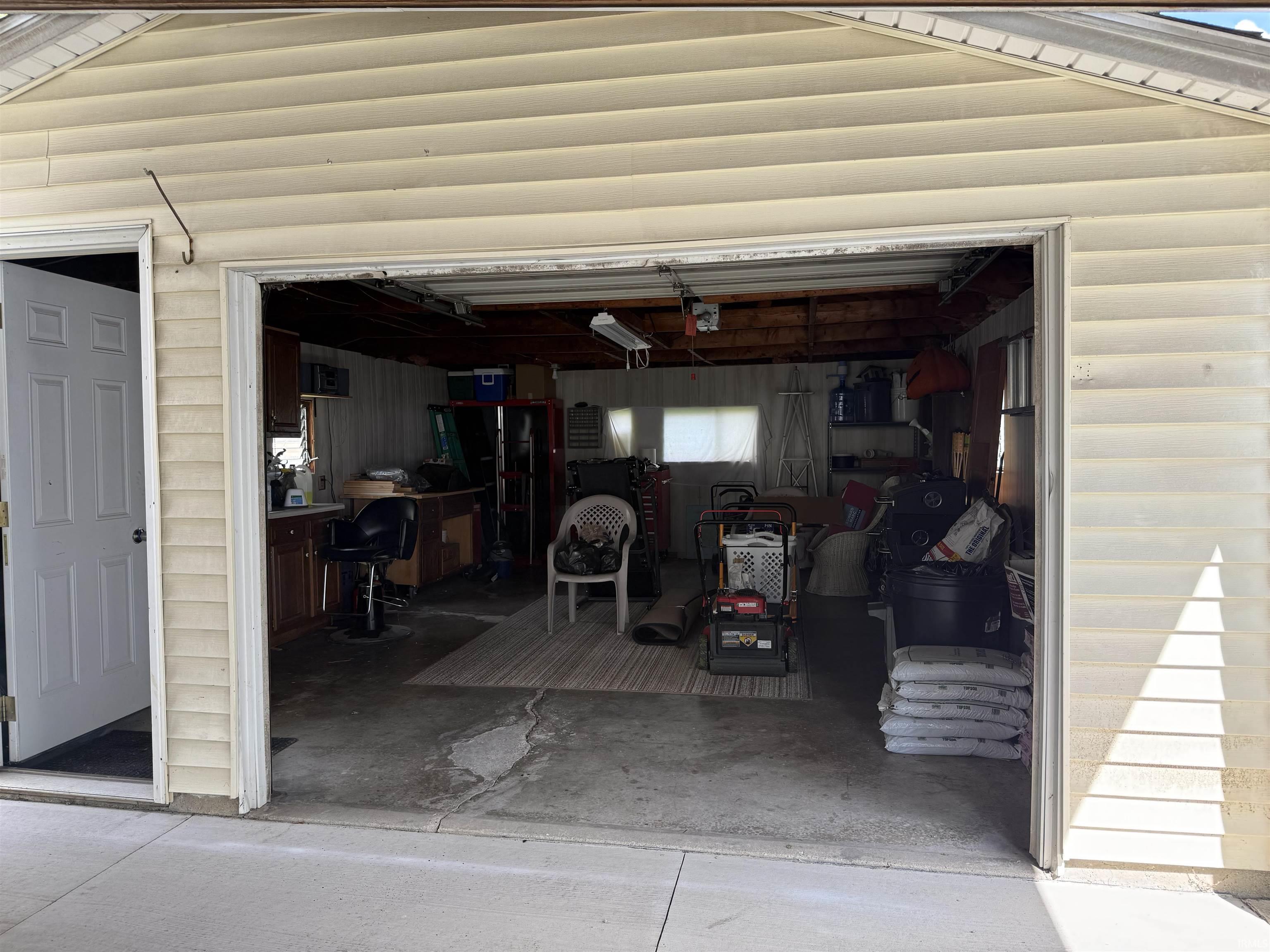 Attached two-car garage with overhead door opening, featuring light-colored vinyl siding and an entry door