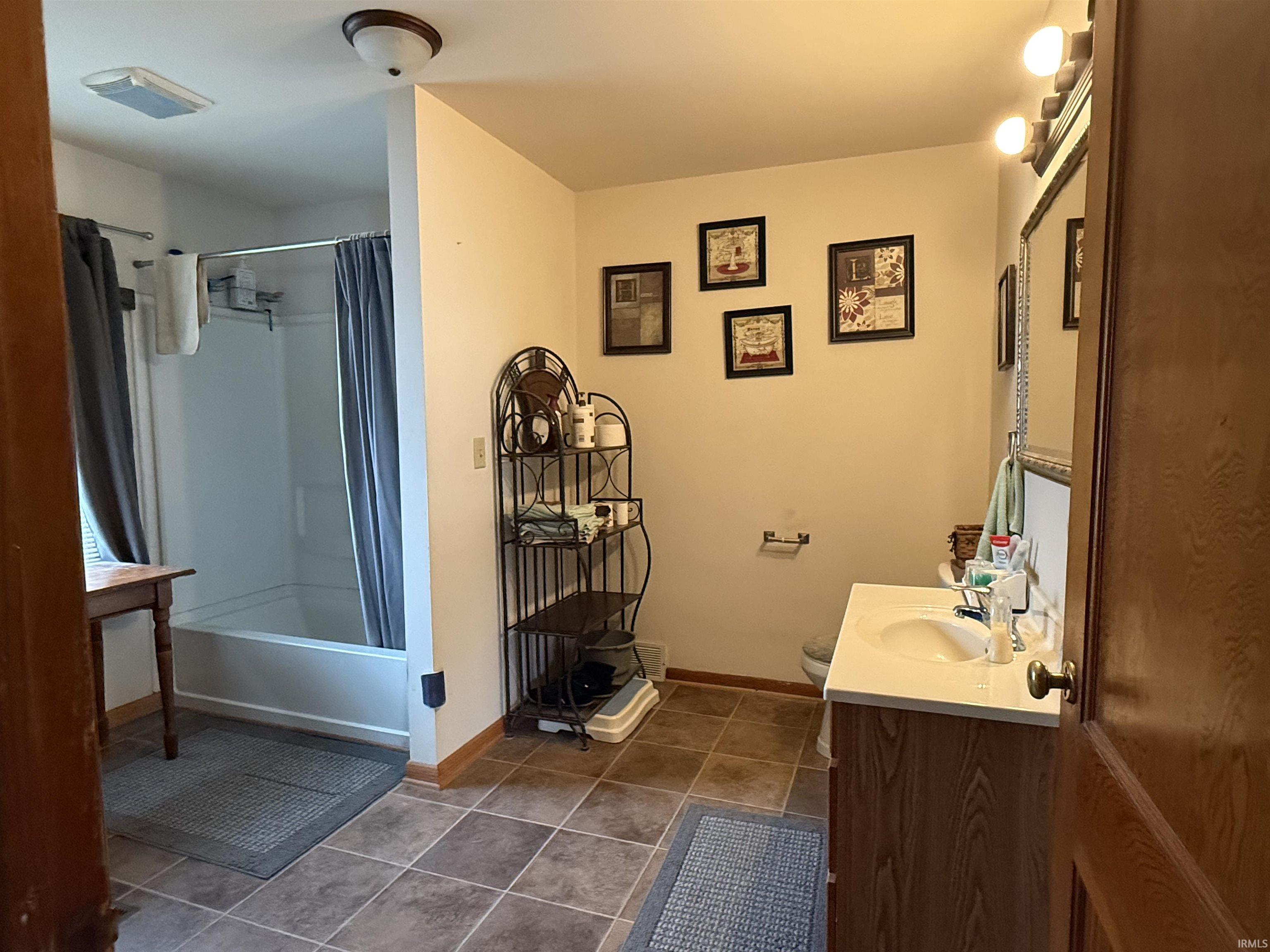Bathroom featuring a white bathtub/shower combination, a vanity with a white countertop and integrated sink, a wall-mounted medicine cabinet, and brown tile flooring
