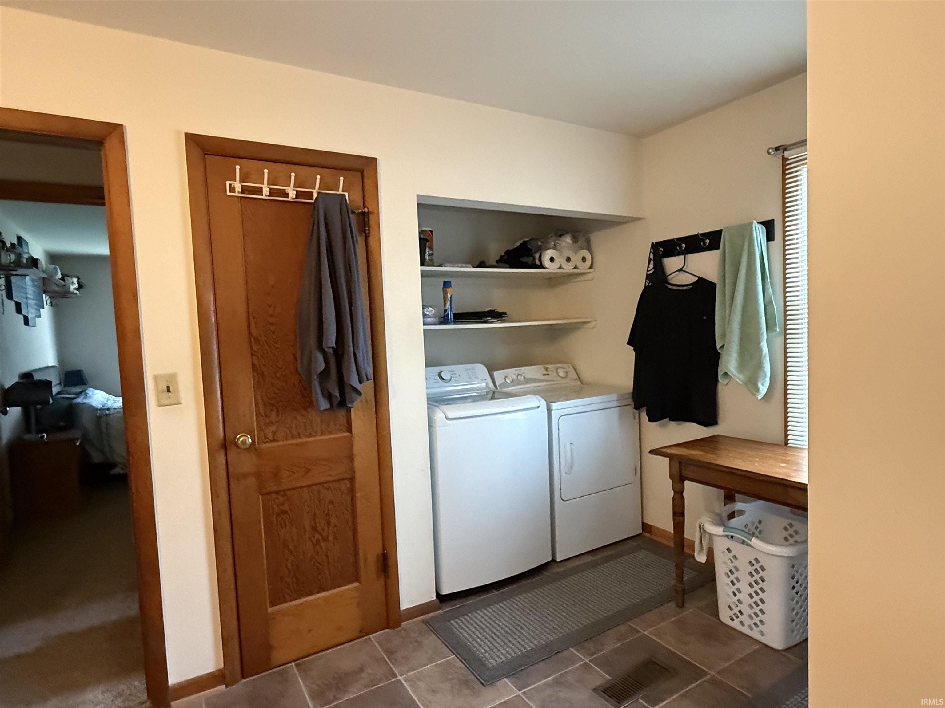Dedicated laundry area featuring a washer and dryer, built-in shelving, and tiled flooring
