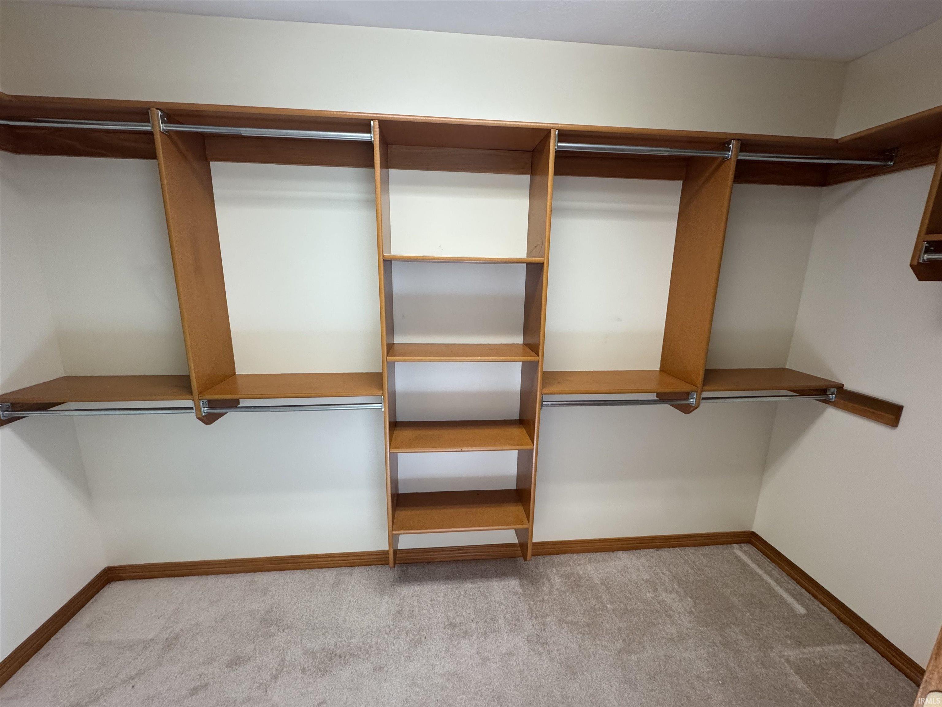 Spacious closet featuring custom wood-finish shelving and multiple hanging rods