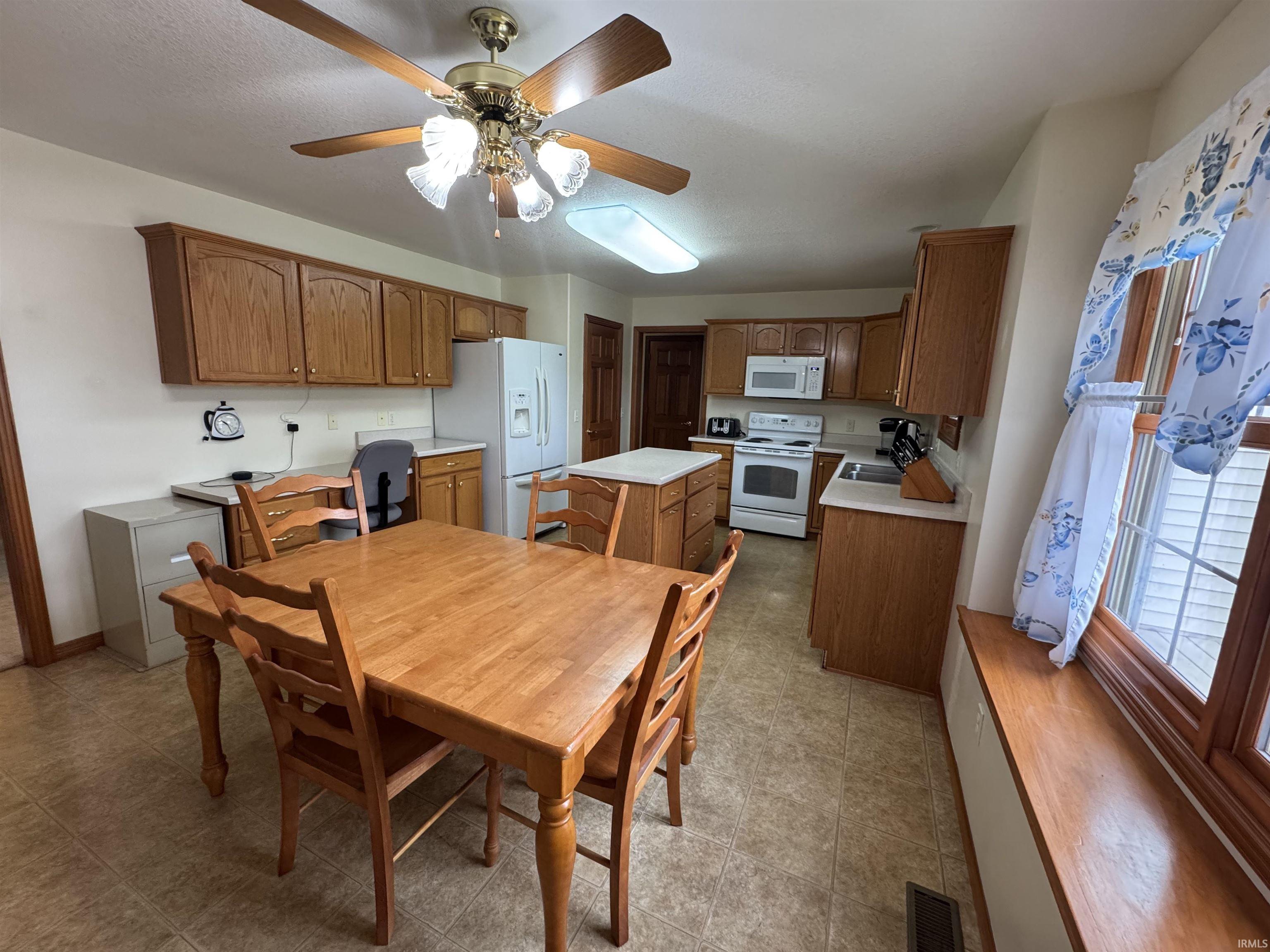 Spacious kitchen featuring wood cabinetry, a central island, and white appliances