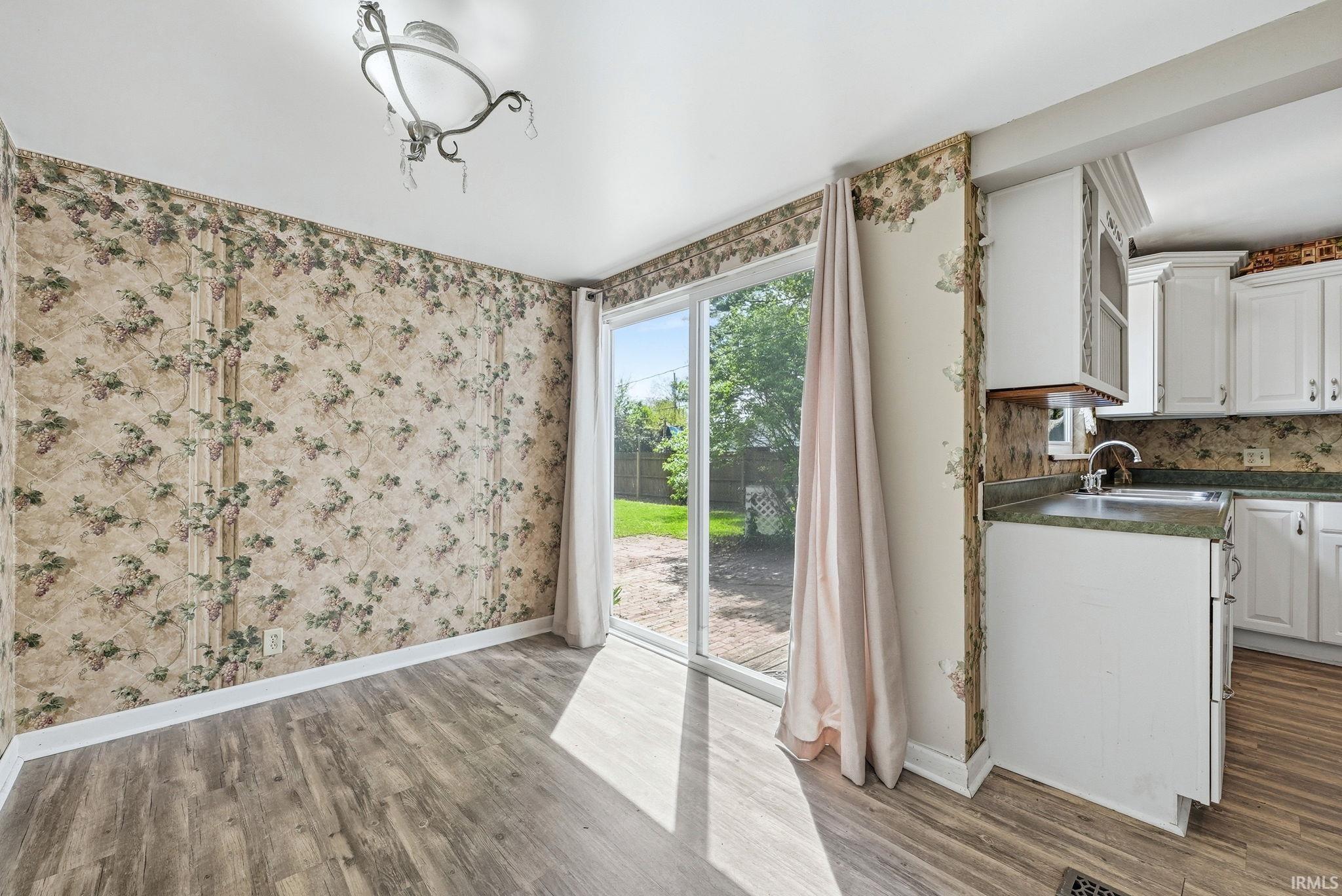 Expansive room featuring wood-finish flooring, a decorative ceiling fixture, and a sliding glass door providing direct outdoor access to a private backyard