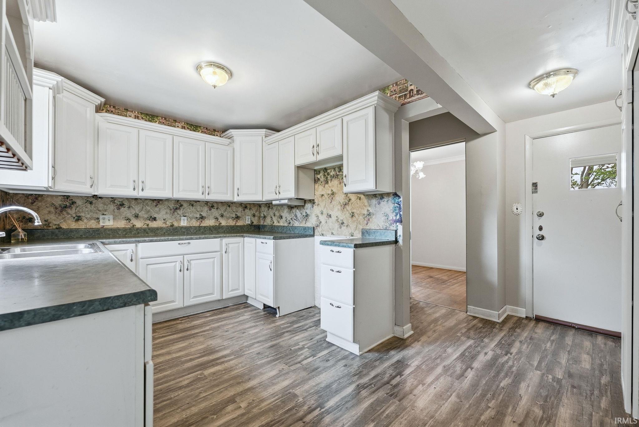 Kitchen featuring white cabinetry, dark countertops, wood-finish flooring, and a stainless steel sink with a high-arch faucet