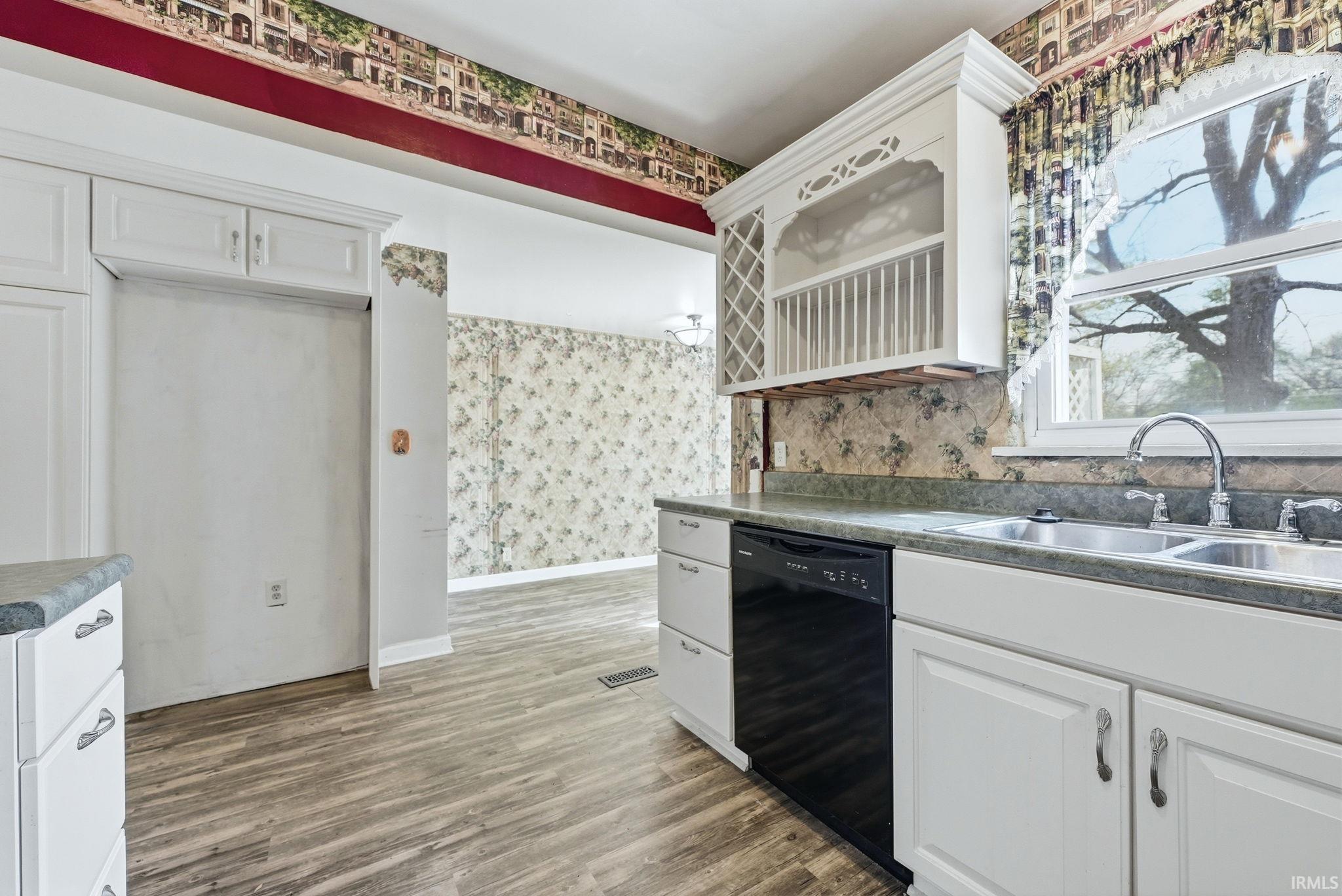 Kitchen space featuring wood-finish flooring, white cabinetry, dark countertops, and a double basin sink
