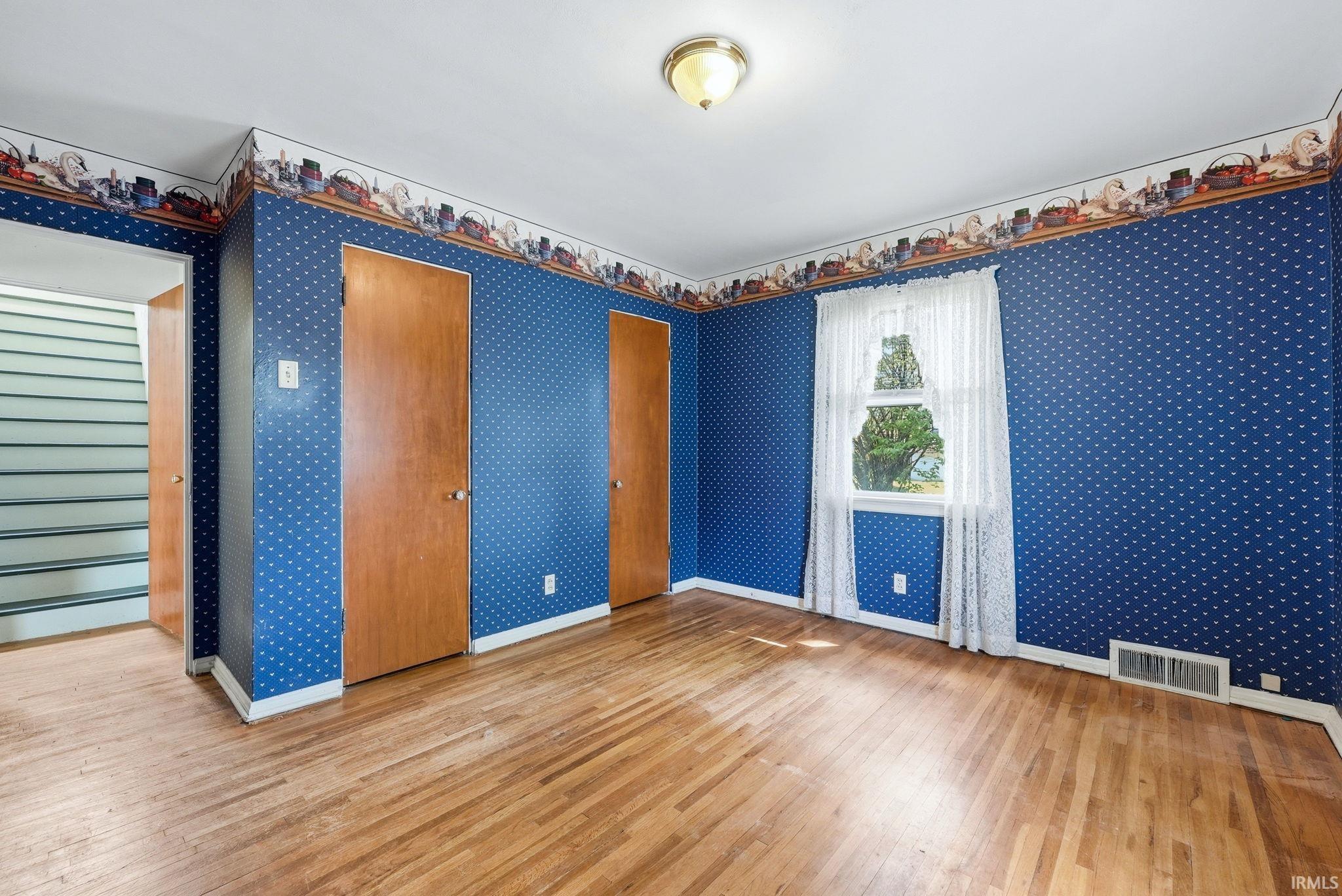 Hardwood flooring extends throughout this room, featuring a window with natural light and two wood-paneled doors