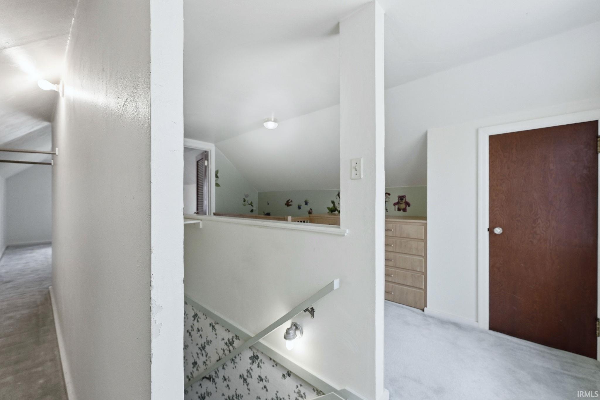 Upper-level hallway featuring sloped ceilings, light-colored carpeting, and a dark wood-finish door
