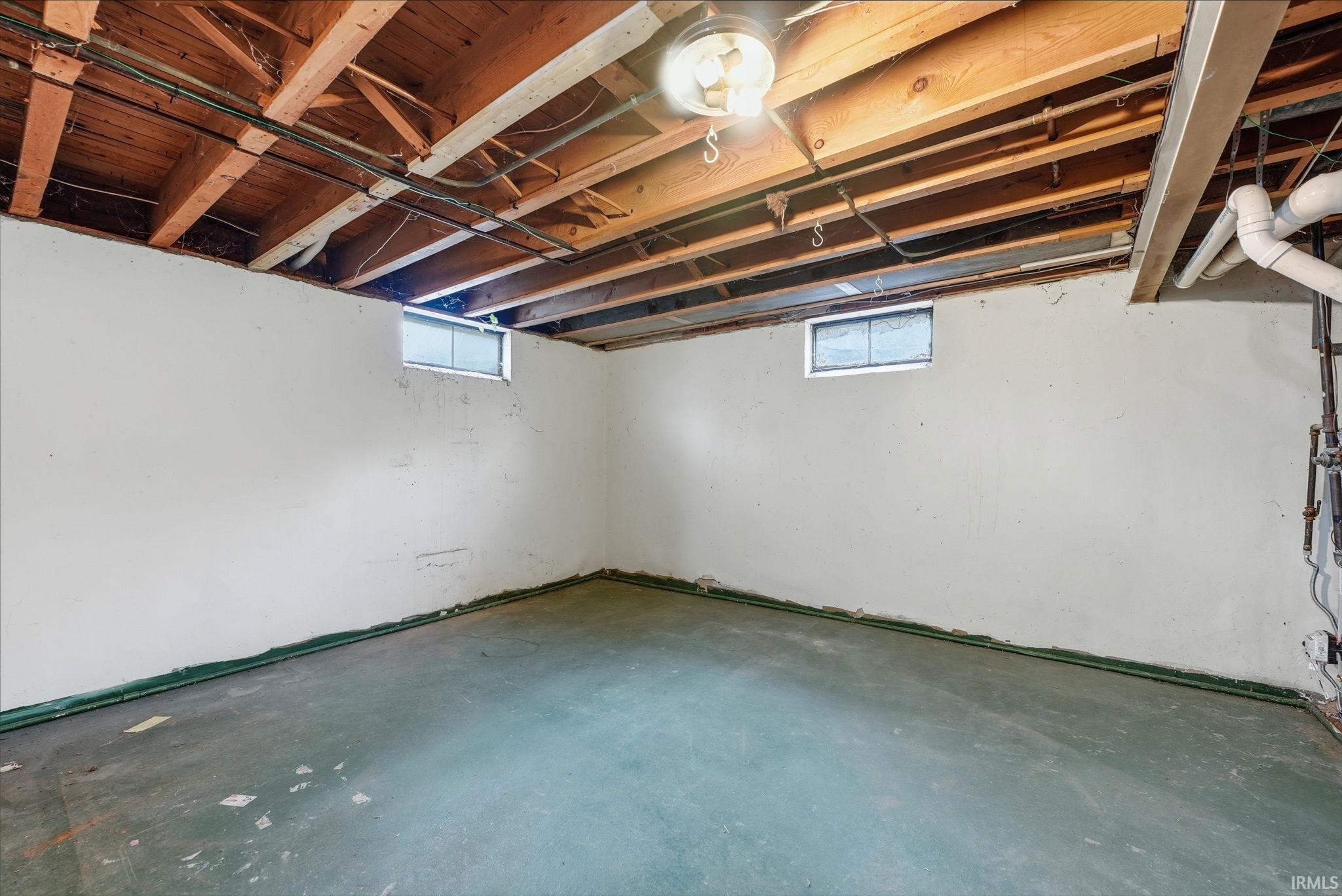 Unfinished lower level featuring concrete flooring, painted foundation walls, exposed ceiling joists, and two high-set windows