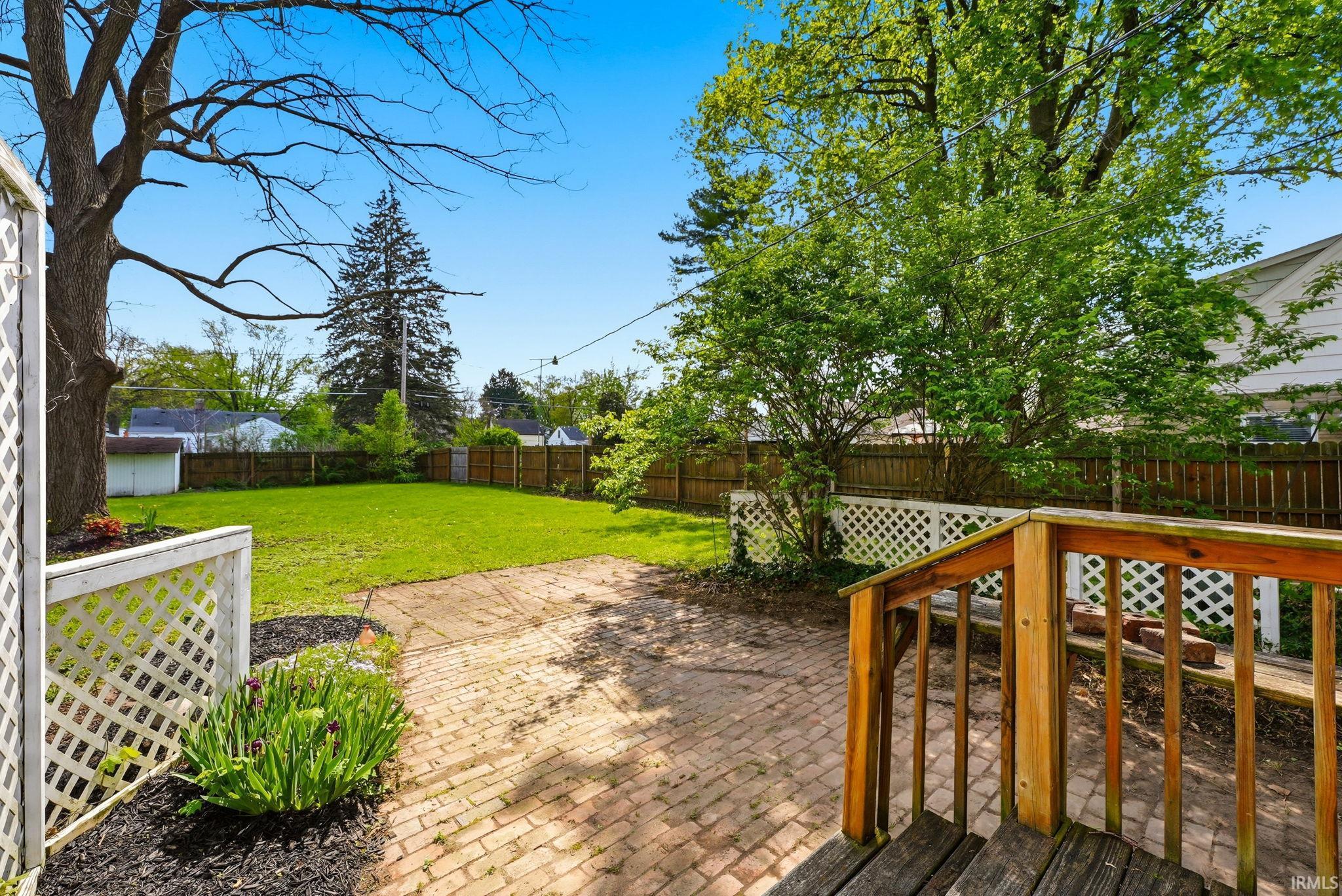 Expansive backyard featuring a brick patio, lush green lawn, mature trees, and privacy fencing