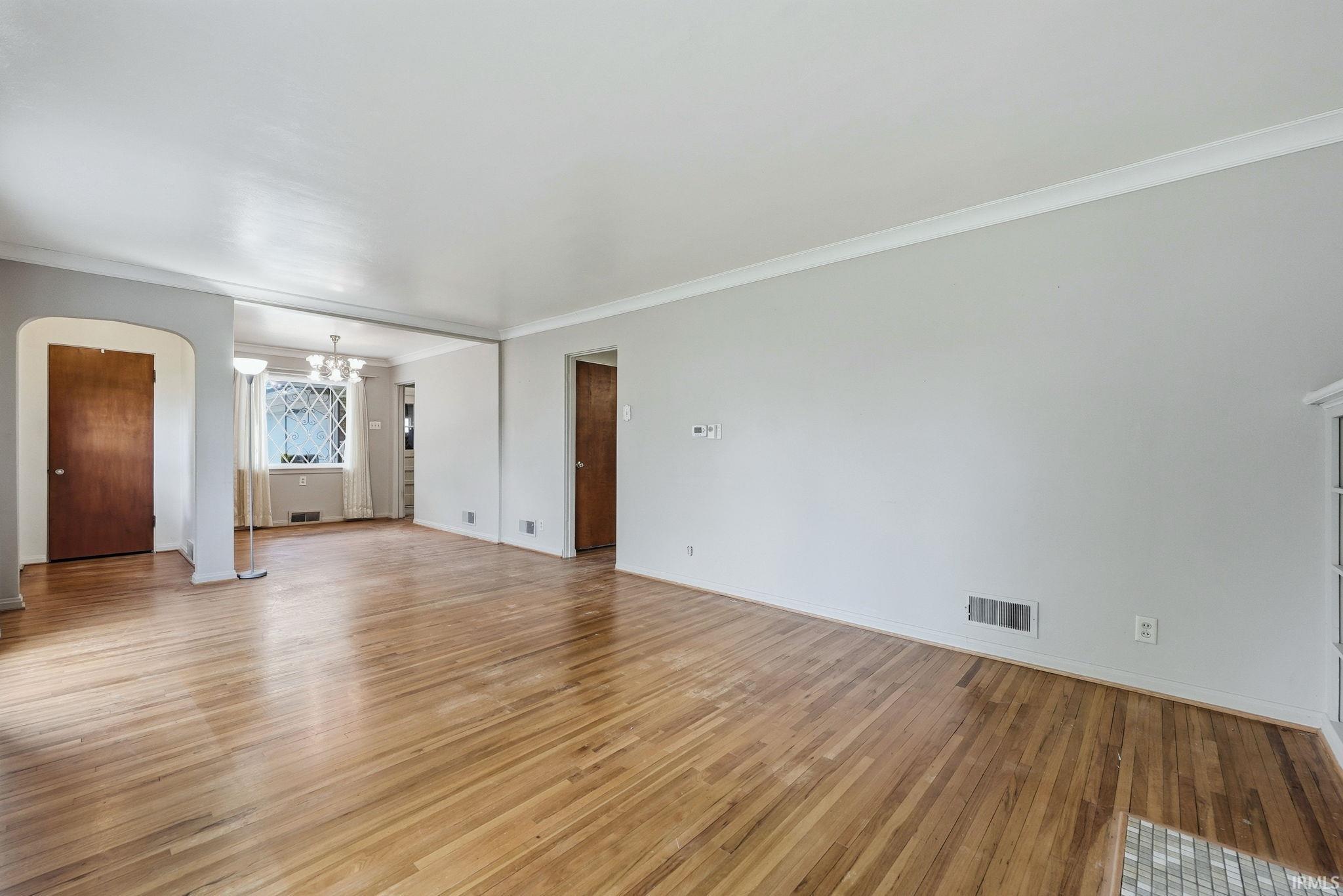 Expansive living area featuring wood flooring, neutral wall tones, white crown molding, and an arched entry