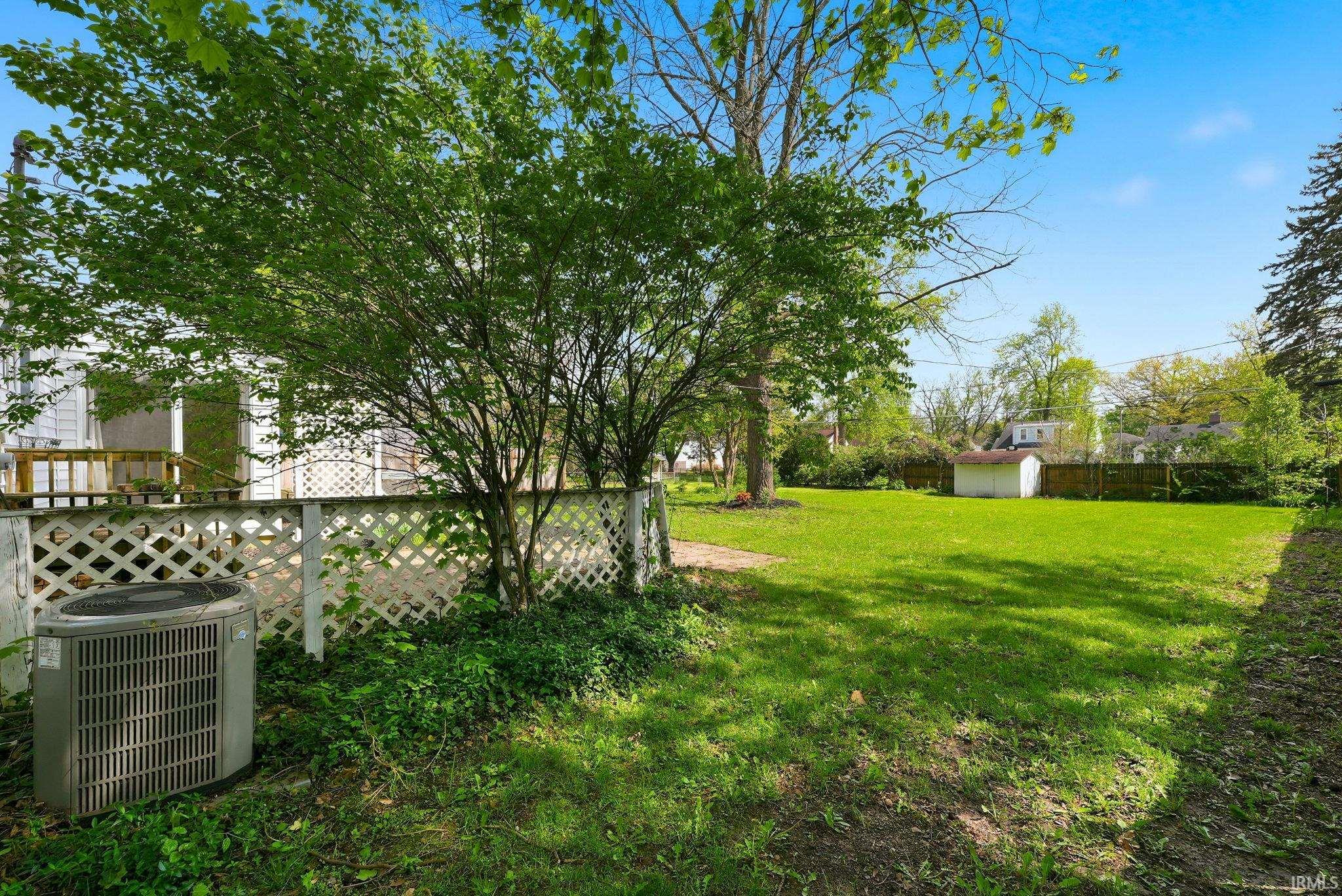 Expansive rear yard featuring a manicured lawn, mature trees, and a white lattice fence