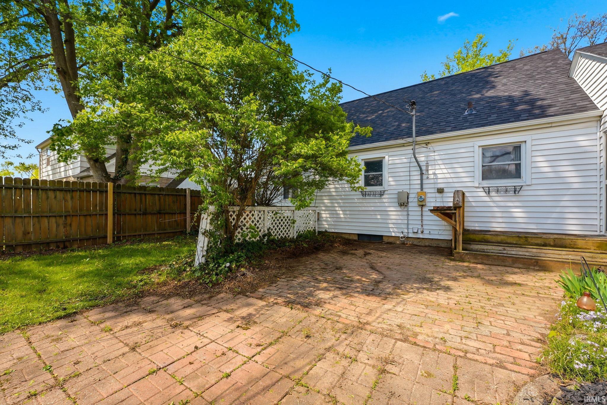Brick paver patio with a garden bed, partially enclosed by a privacy fence and lattice work