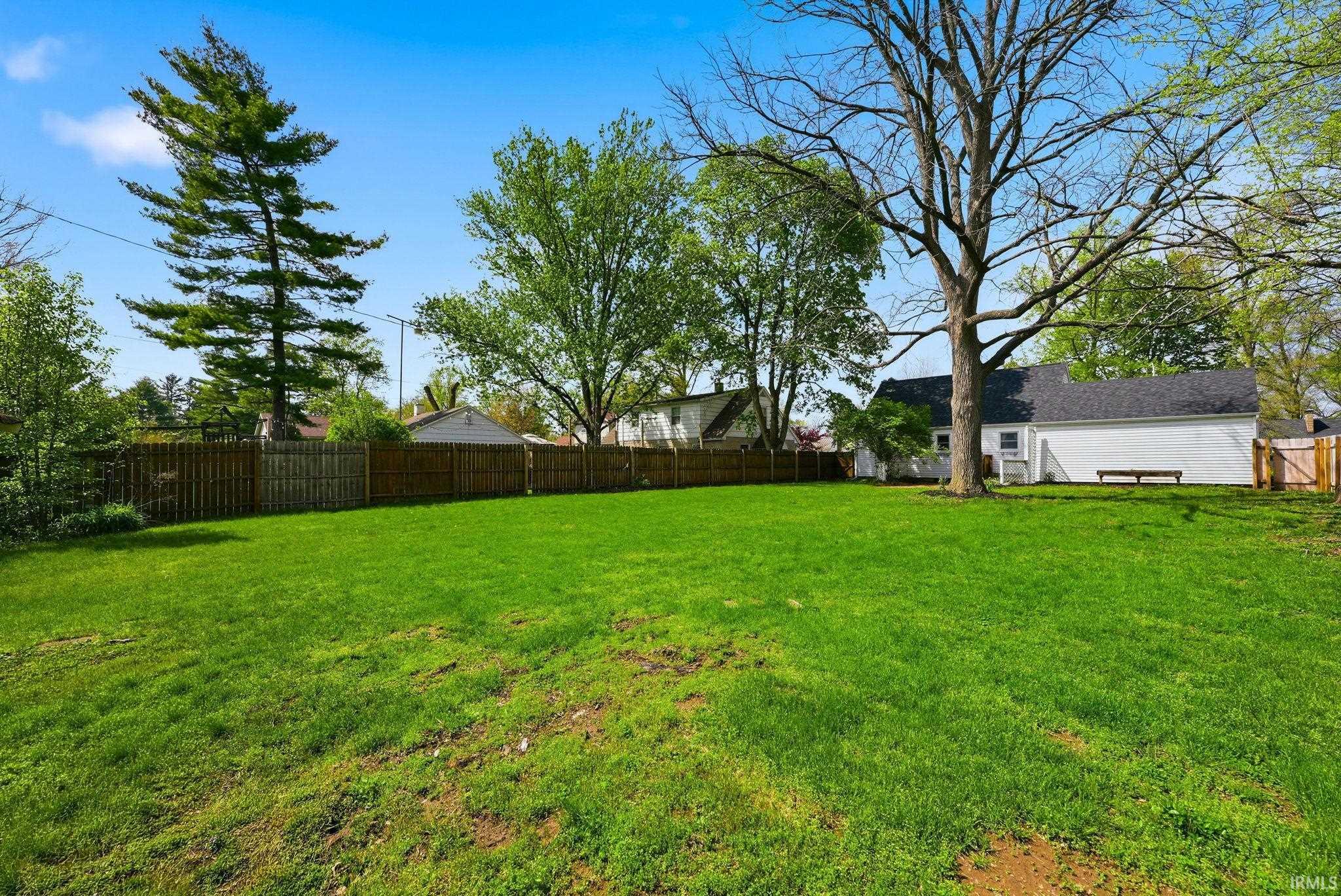 Expansive grassy yard area featuring a full perimeter privacy fence and mature trees