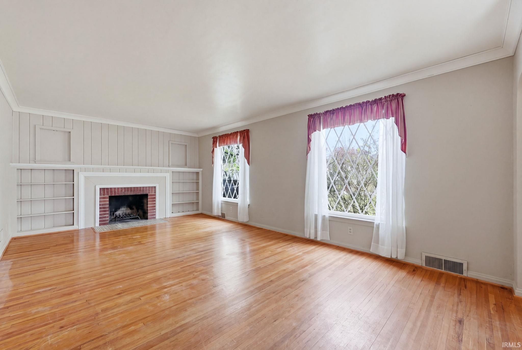 Spacious room featuring wood-finish flooring, a red brick fireplace with a white mantel, and built-in shelving